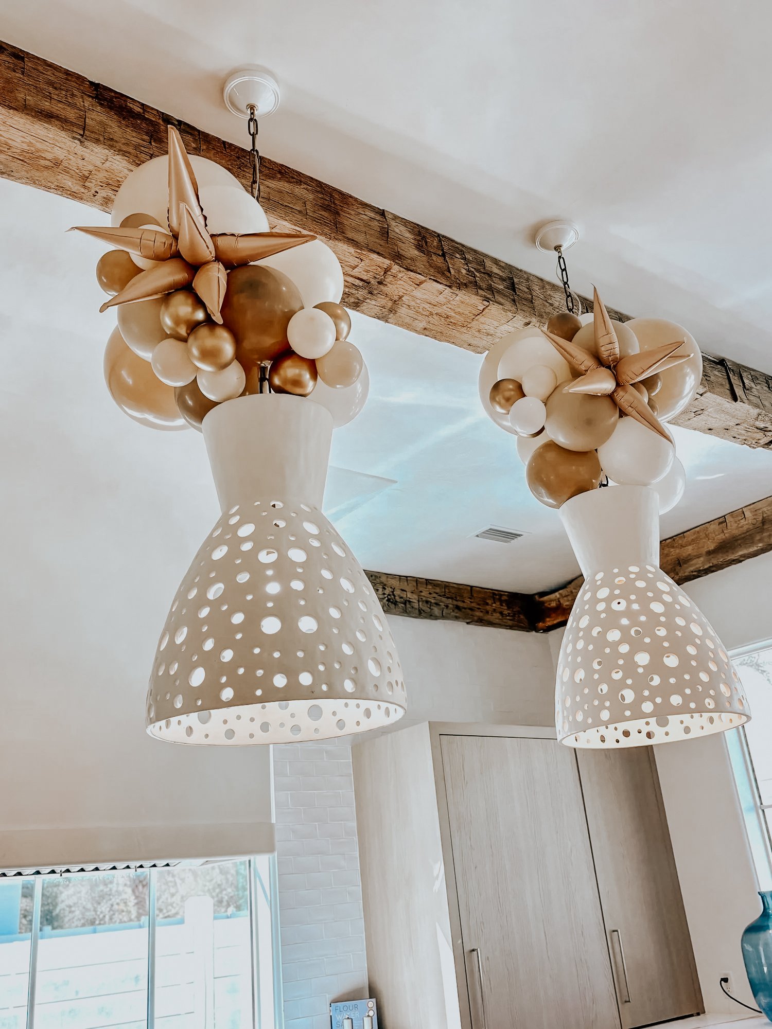 Balloon and star-shaped balloon clusters hanging from ceiling lights for a 30A indoor celebration.