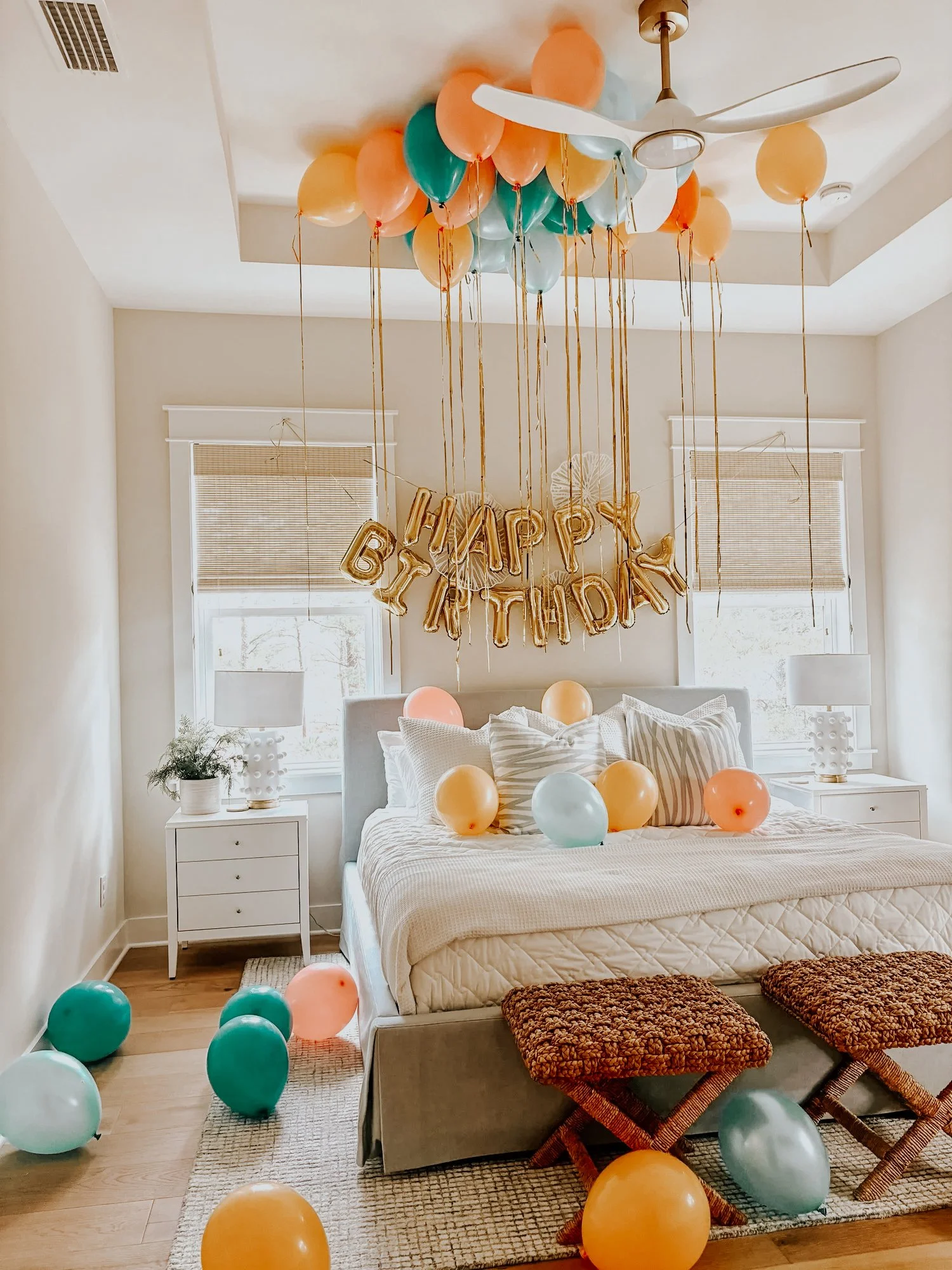 Birthday surprise setup with colorful ceiling balloons, floor balloons, and a gold “Happy Birthday” banner styled in a 30A vacation rental bedroom.