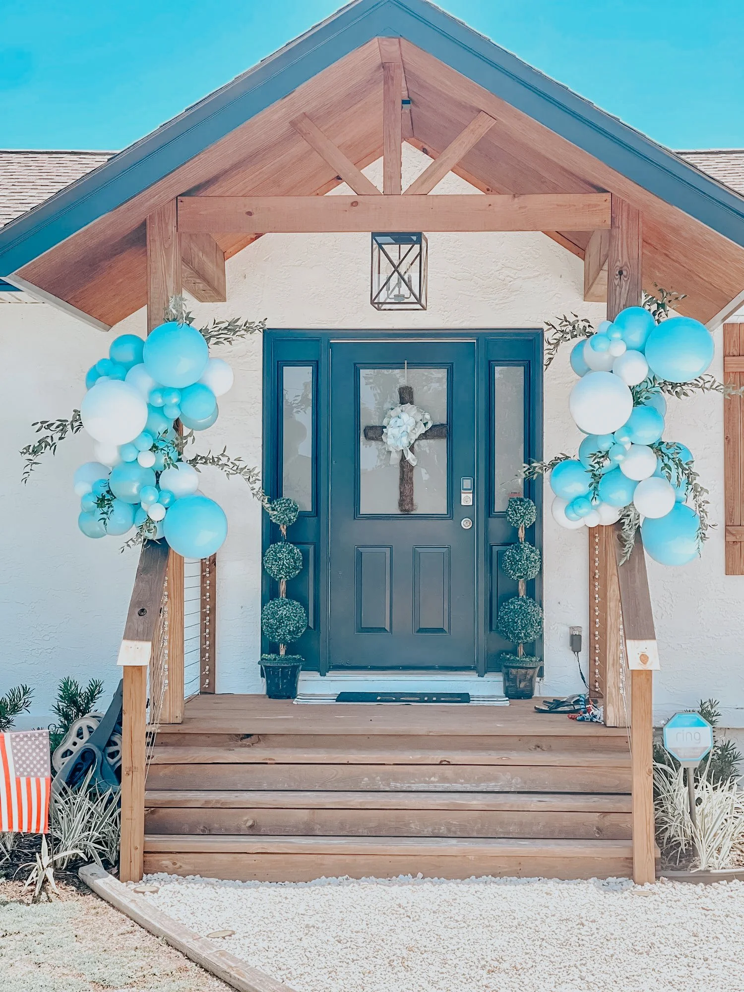 Blue and white balloon décor with florals styled on a 30A front porch for a baby shower celebration or religious event.
