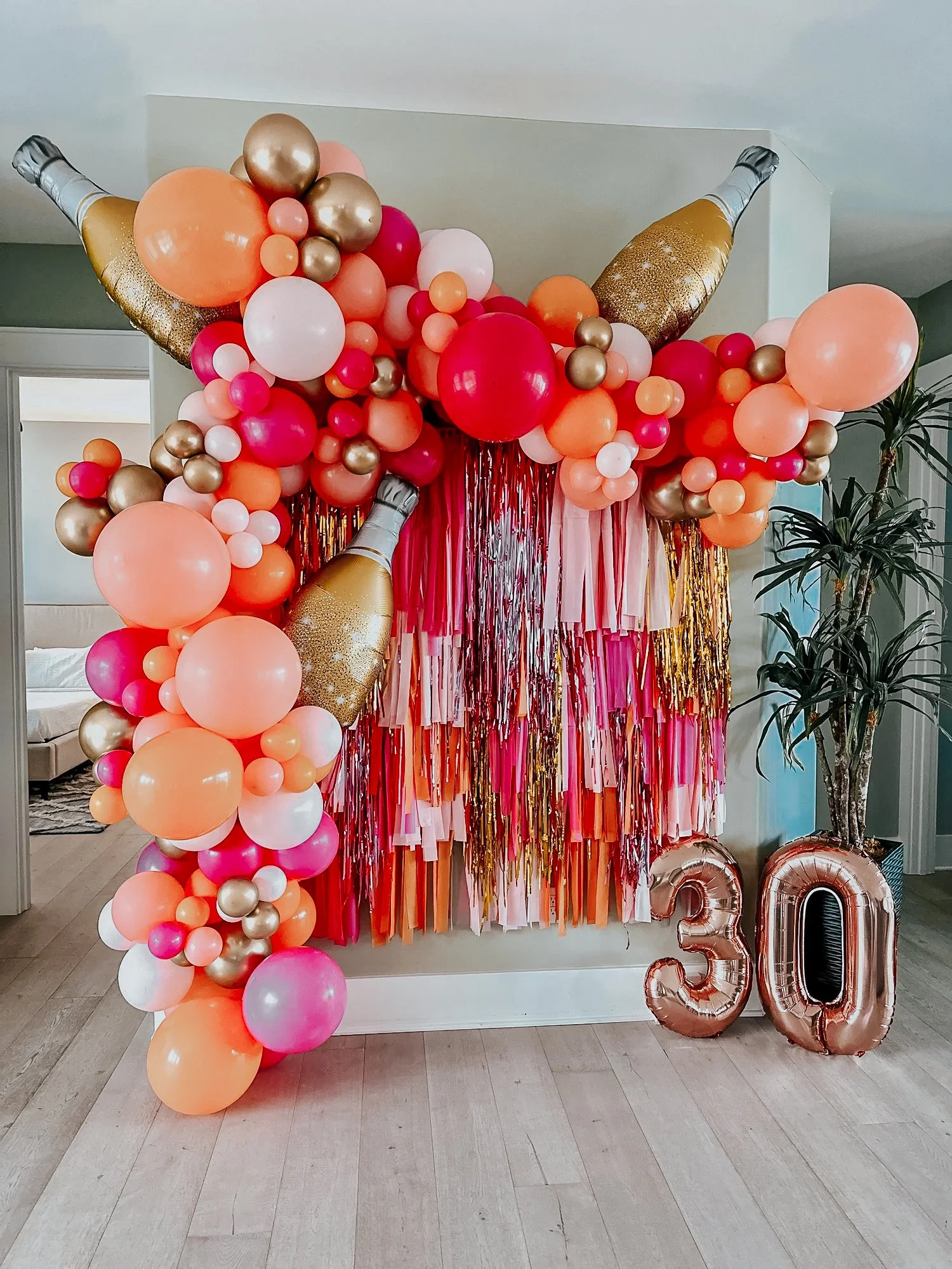 Pink, orange, white, and gold balloon décor with streamers, champagne bottle balloons, and large “30” foils styled for a 30A 30th birthday celebration.
