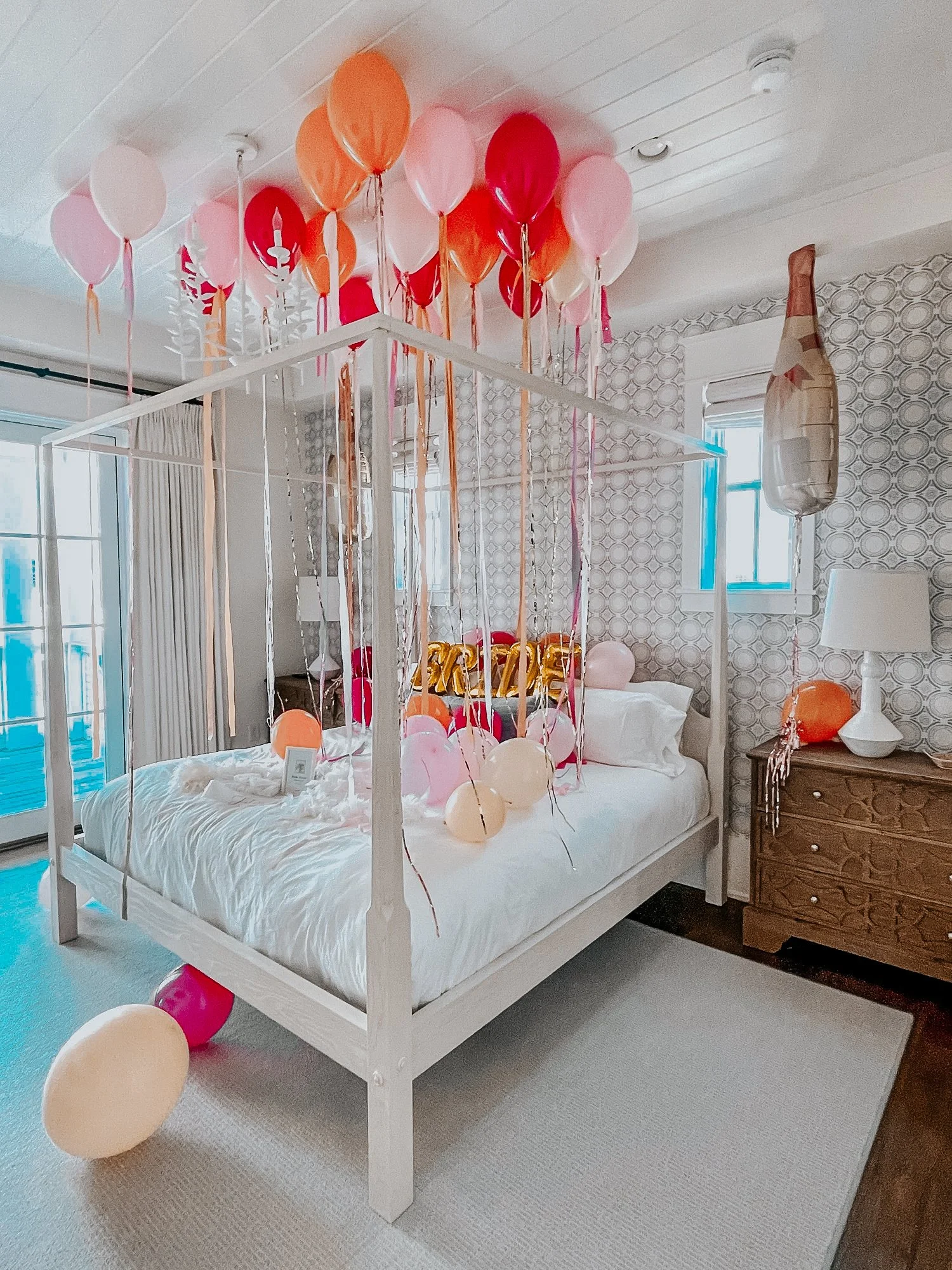 Bridal surprise setup with pink and orange ceiling balloons and floor balloons styled in a 30A vacation rental bedroom.
