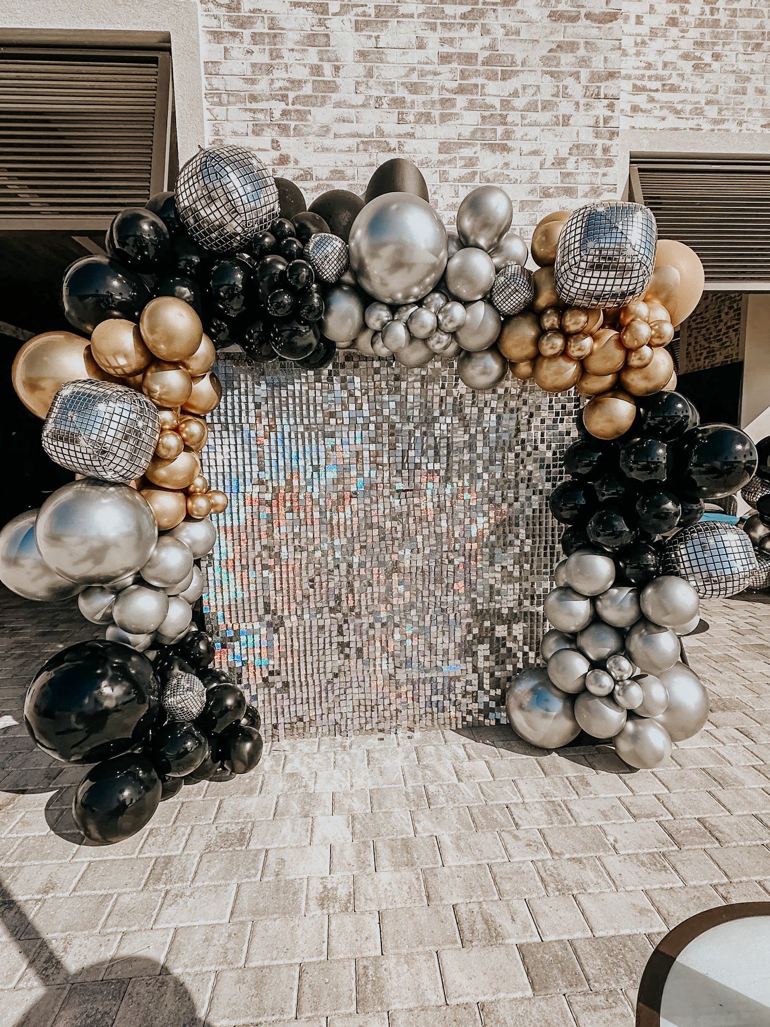 Black, silver, and gold balloon arch framing a shimmer mosaic backdrop (shimmer wall) for a 30A outdoor celebration or corporate event.