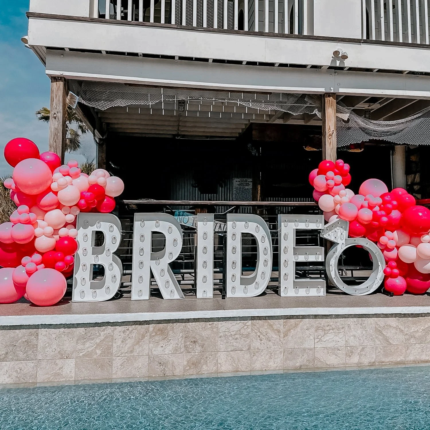 Large white “BRIDE” letters surrounded by pink balloon décor for an outdoor 30A bridal celebration.