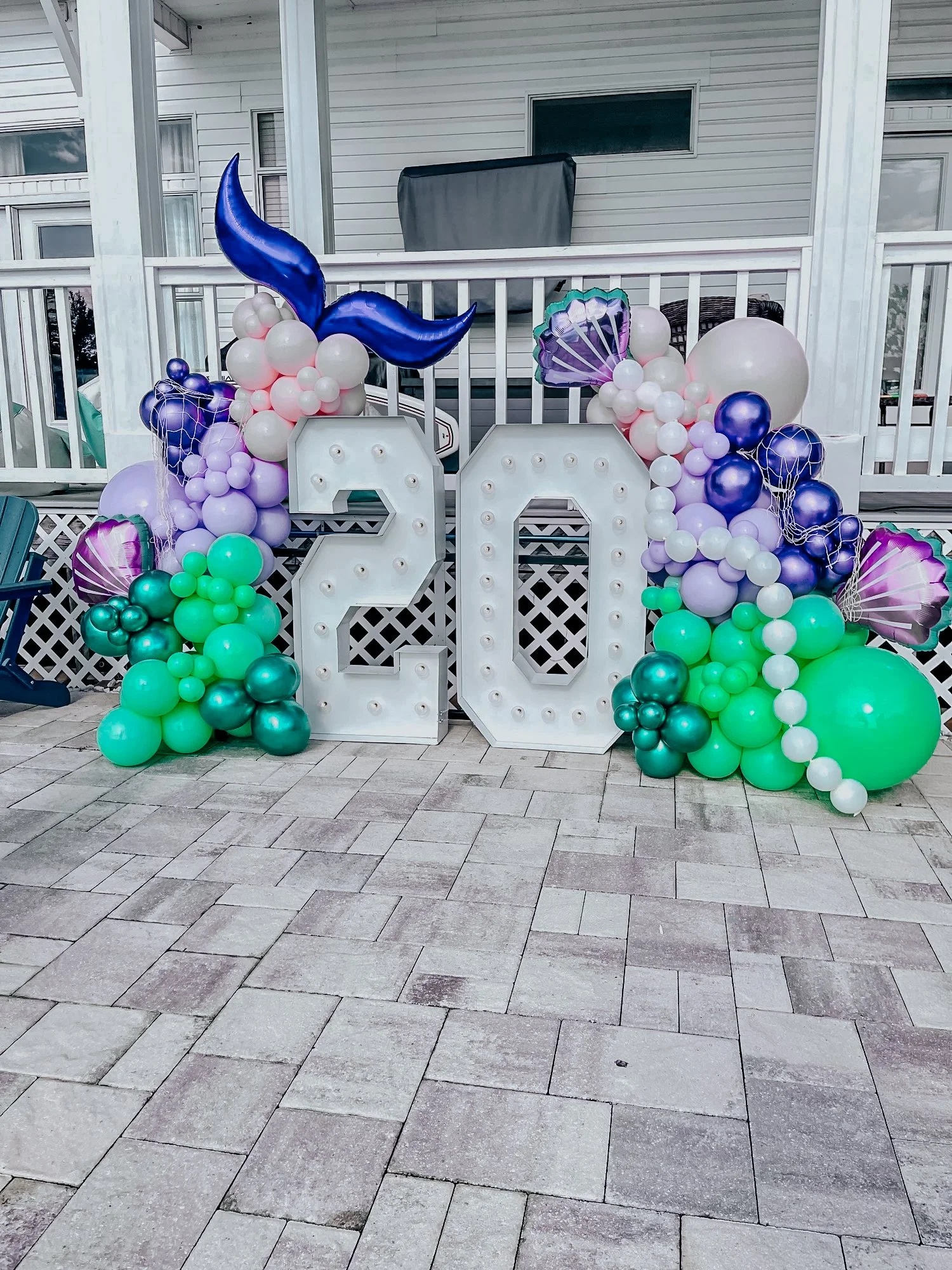 Illuminated “20” marquee surrounded by pastel purple, pink, and green balloon décor with metallic shell accents for a 30A outdoor birthday celebration.