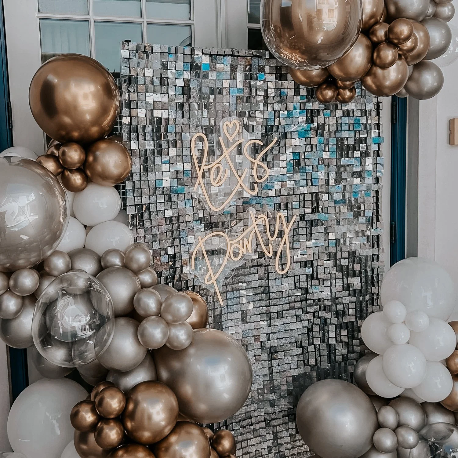 Mirror tile mosaic backdrop with gold, silver, and white balloon décor and a “Let’s Party” neon sign for a 30A celebration.