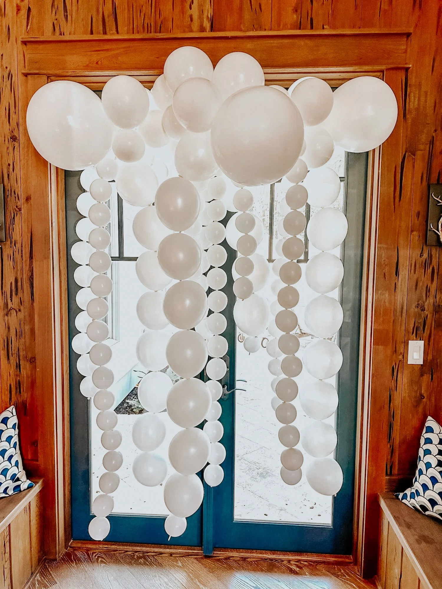 White balloon garland and hanging balloon strands styled in a wooden-paneled room for a 30A bridal shower or wedding morning get-ready space.