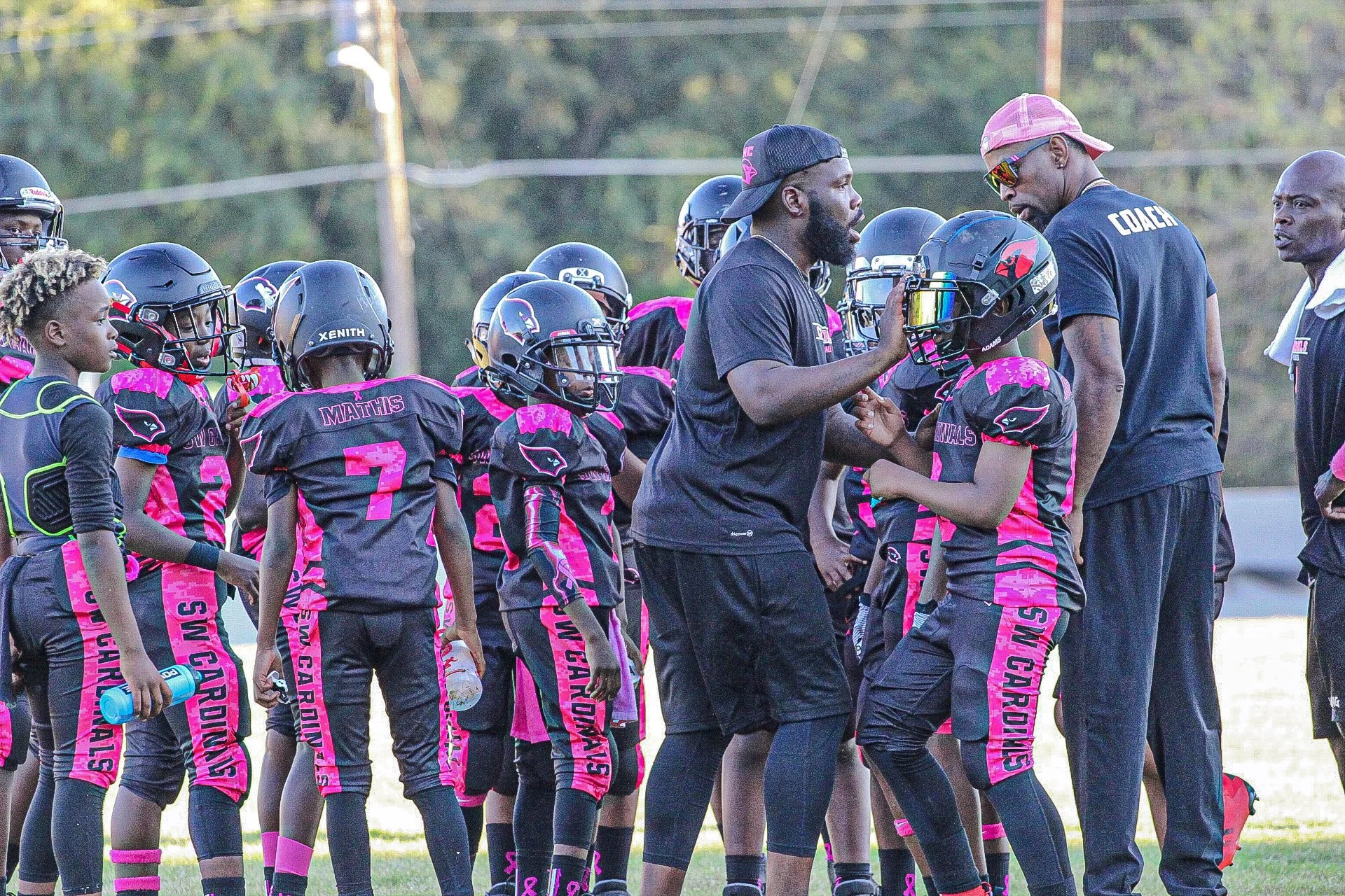Young female football player in pink and black uniform receiving instructions from male coach with clipboard during a game or practice on the field at sunset.