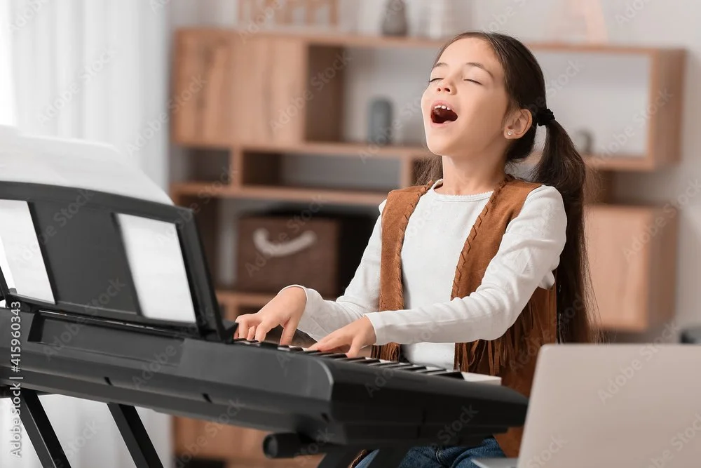 Young girl singing with eyes closed while playing a keyboard in a cozy room.