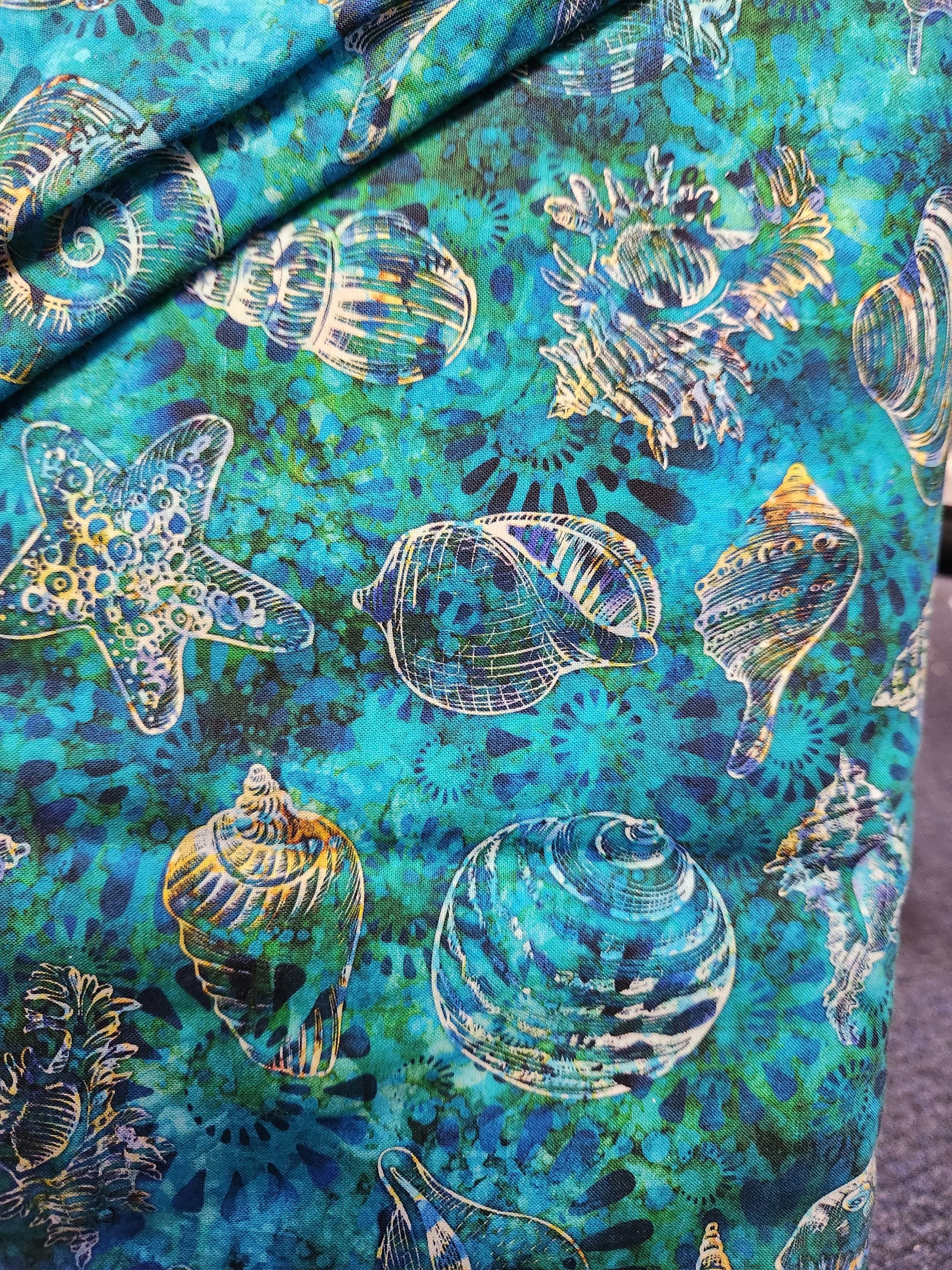 QT Fabrics Pacifica 2600-28818-q blue green background with a assortment of sea shells