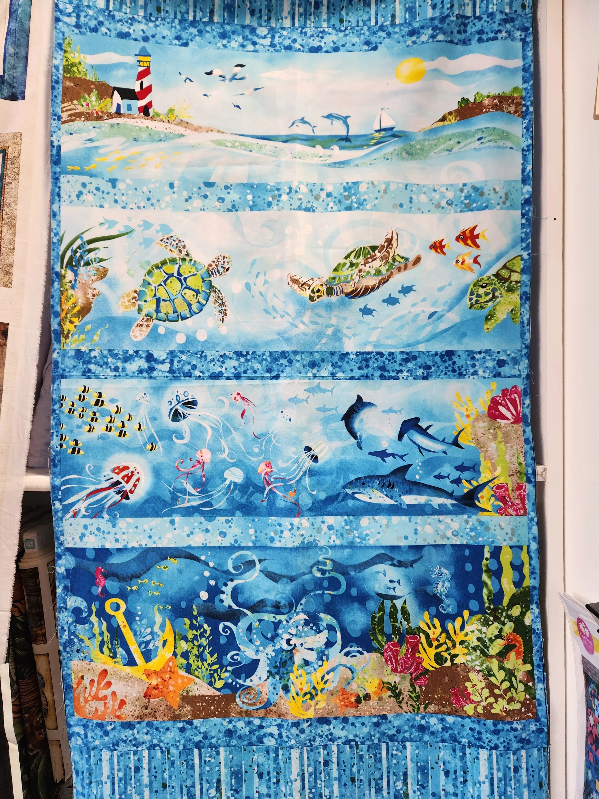 Studio E Ocean State 4503p11 Ocean scenes from the shore and lighthouse to the bottom of the ocean.  The designs are in strips. Bright colors on a medium to light blue background.  Quilting fabric