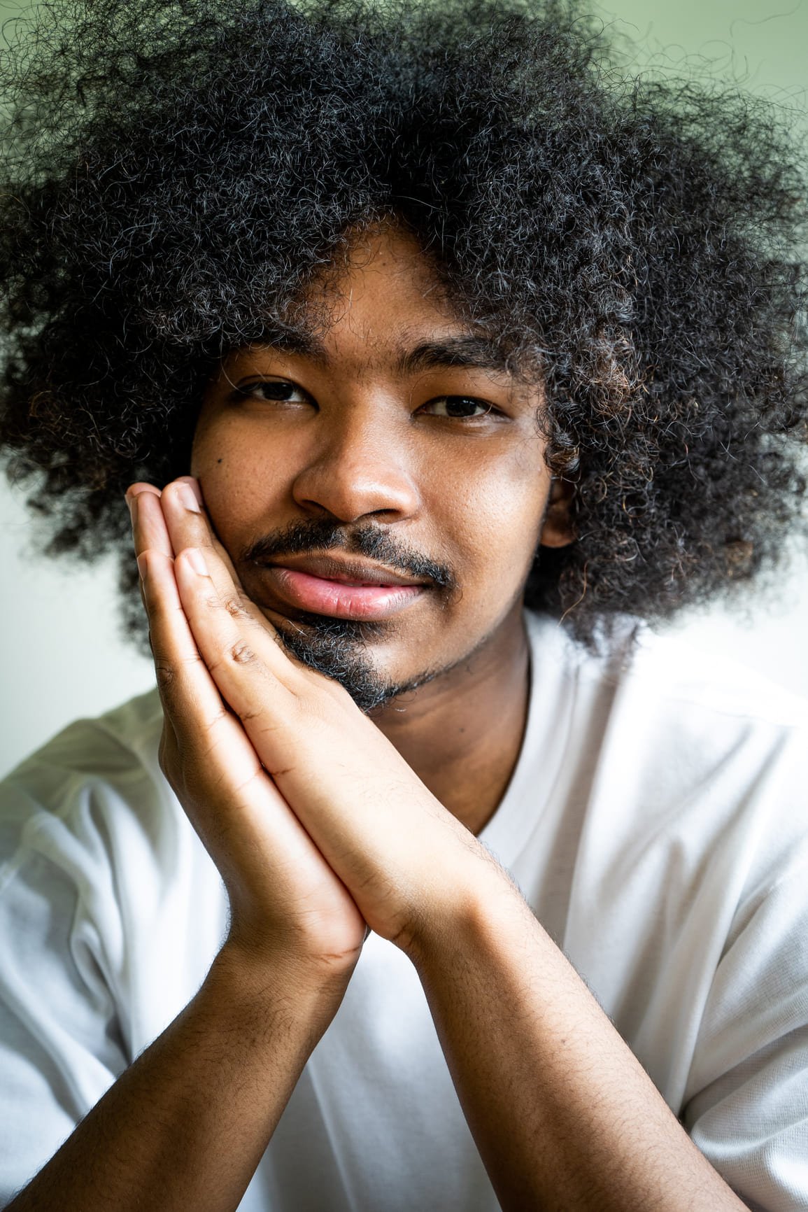 A thoughtful young man stares at the camera, and leans his chin on his hands