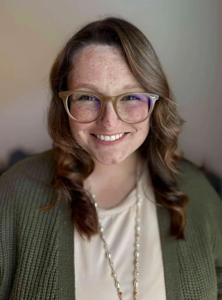 ATX Mental Health therapist Leanne Schutz, LPC-A smiles at the camera in tan glasses and an olive sweater