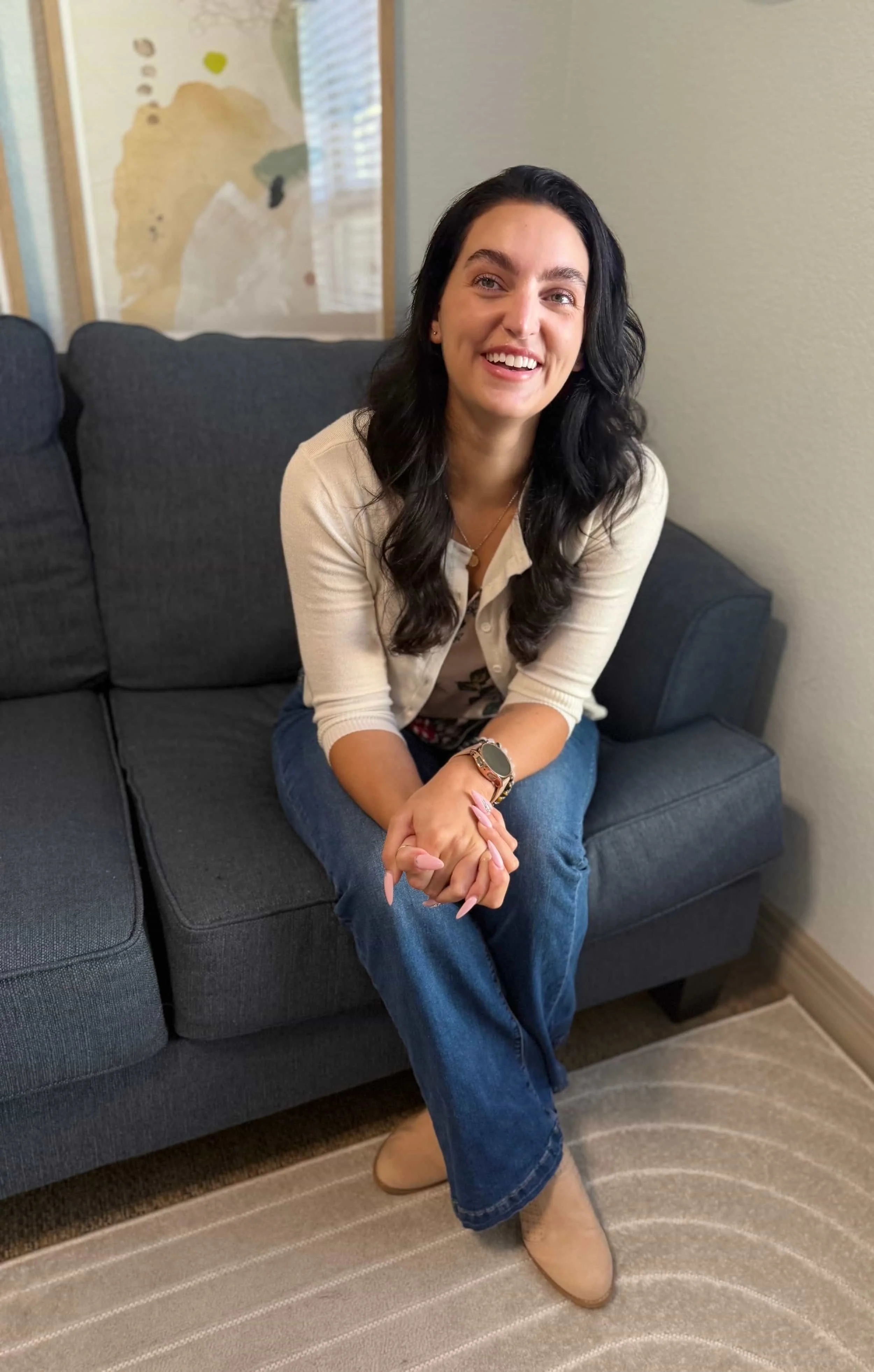 ATX Mental Health therapist Amanda leans towards the camera smiling and sitting on a blue couch