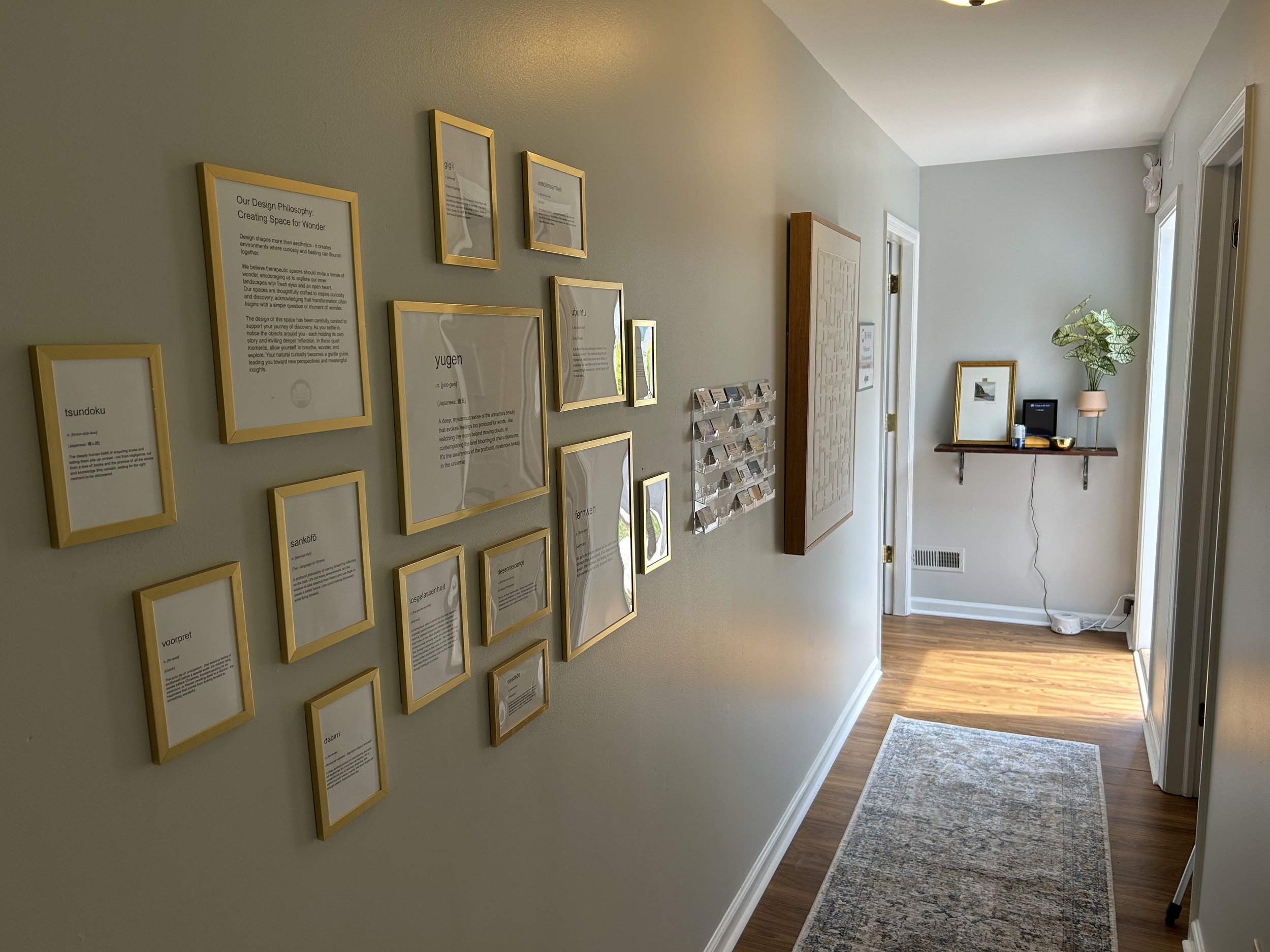Hallway with wall art, wall-mounted shelf with plant and decorations, and a window at the end.