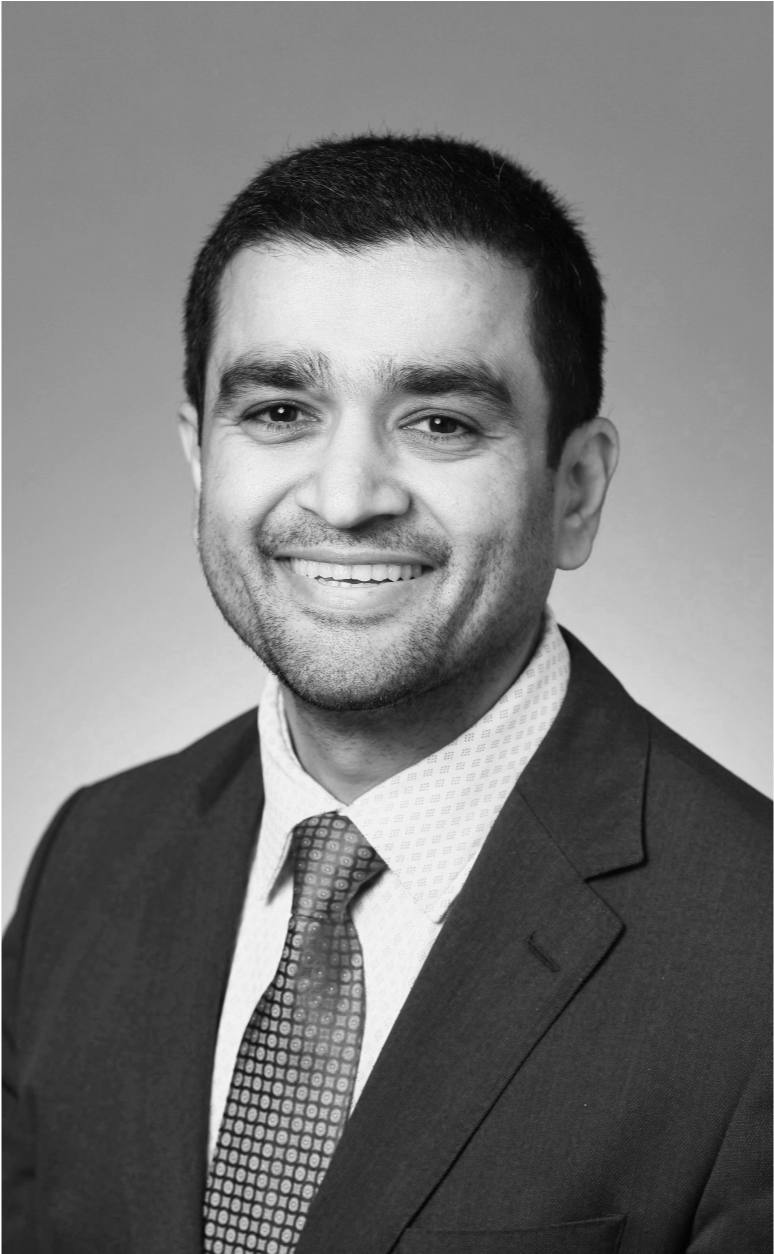 Black and white professional headshot of a smiling man in a suit and tie.