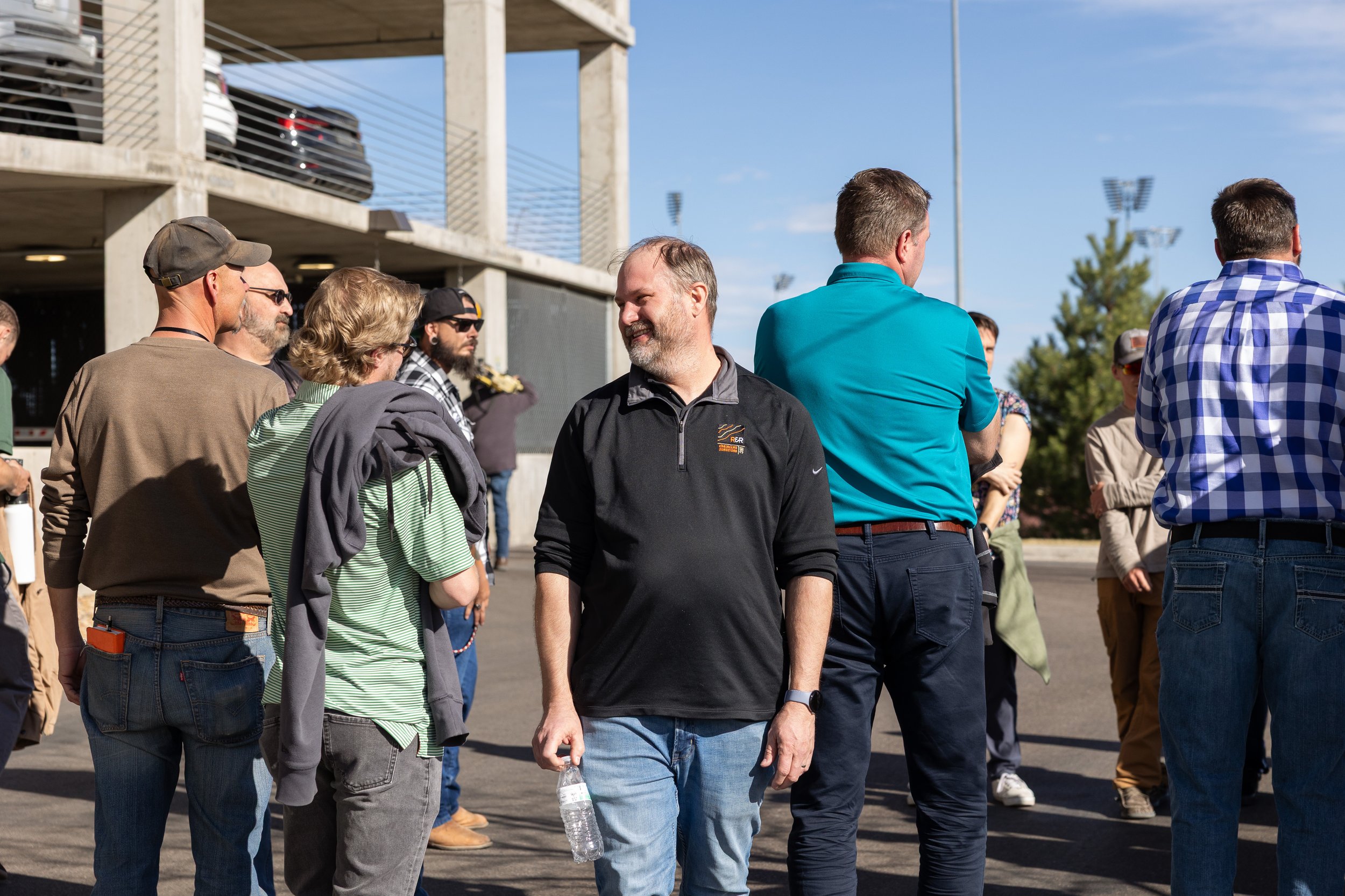 Group of people walking outdoors near a stadium or sports facility on a sunny day.