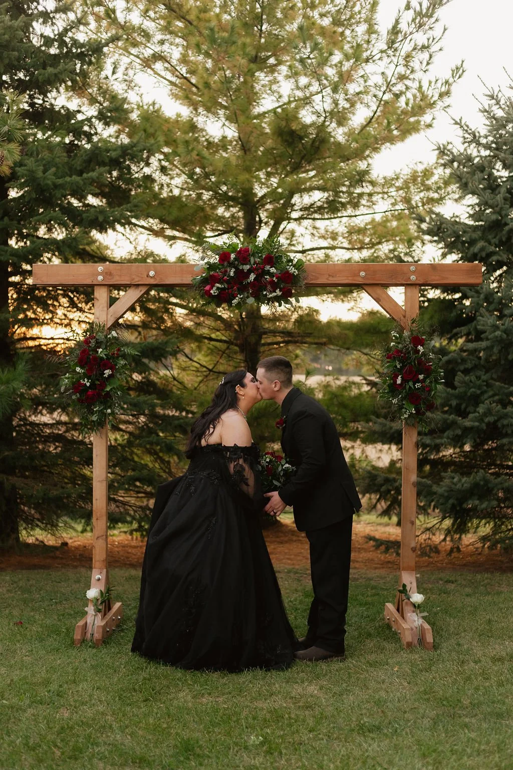 A romantic moment with the bride and groom under the wedding arch decorated wit red rose florals at Country Coach House wedding venue in Burlington, IL.
