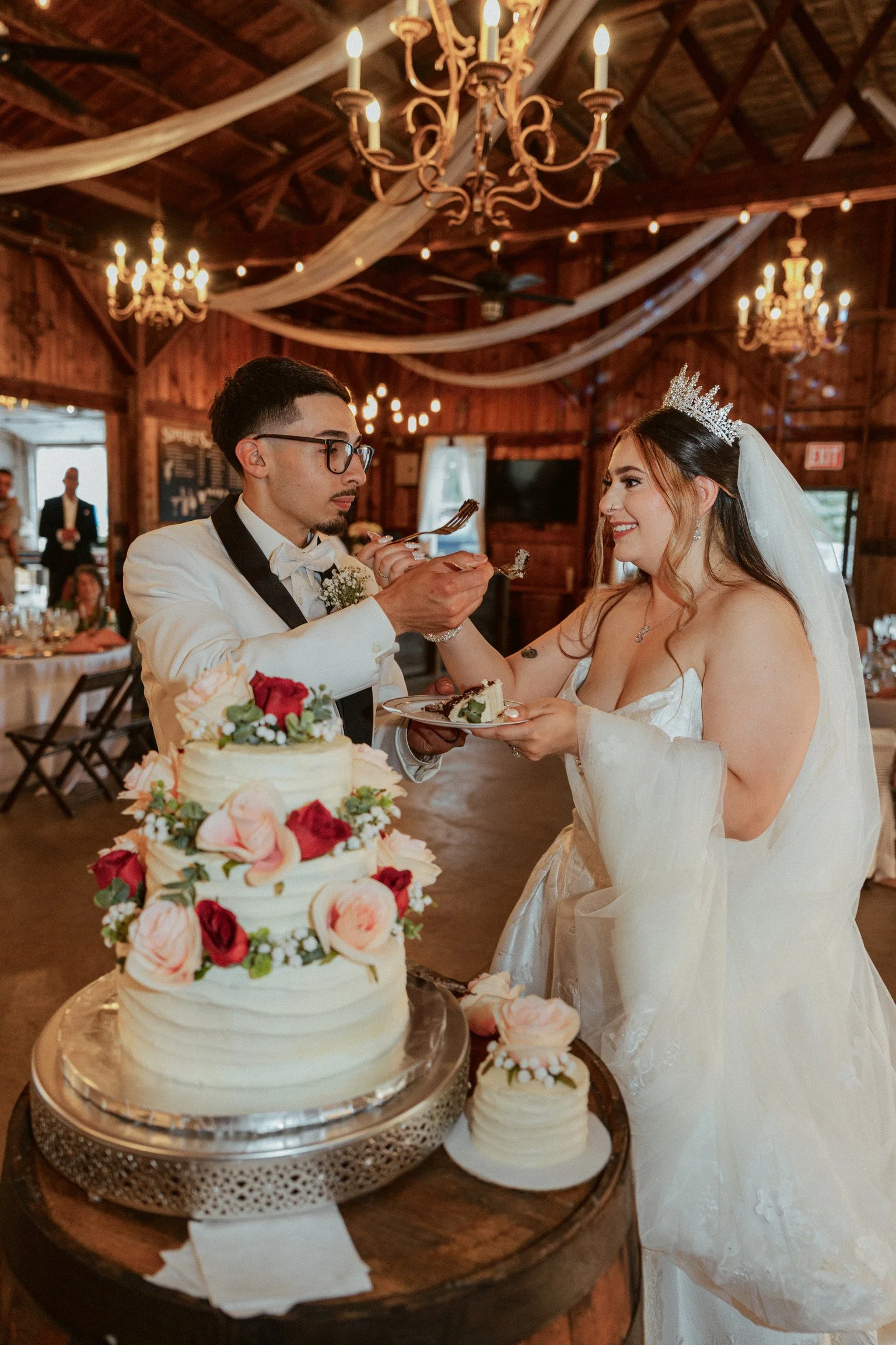 The couple cutting the beautiful  wedding cake garnished with pink and red roses at the charming Country Coach House in Burlington, IL