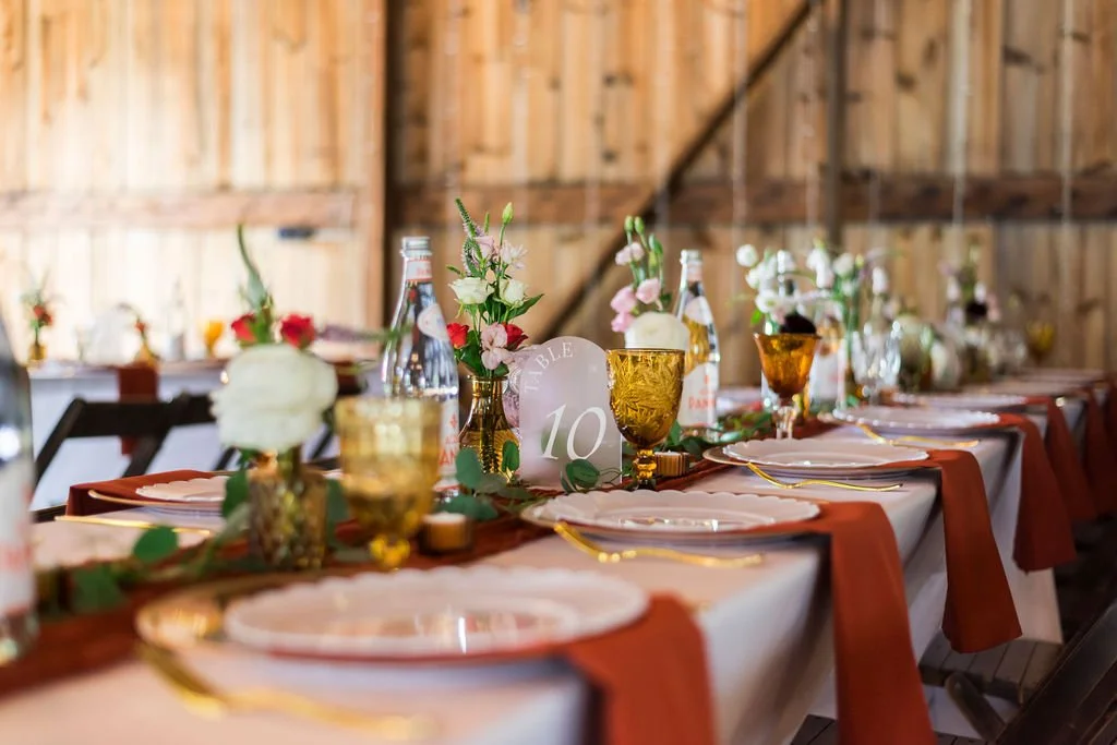 A tablescape with terracotta napkins, candles, greenery, and bud vases created a layered but effortless look at a wedding reception at Country Coach House, in Burlington, IL. .