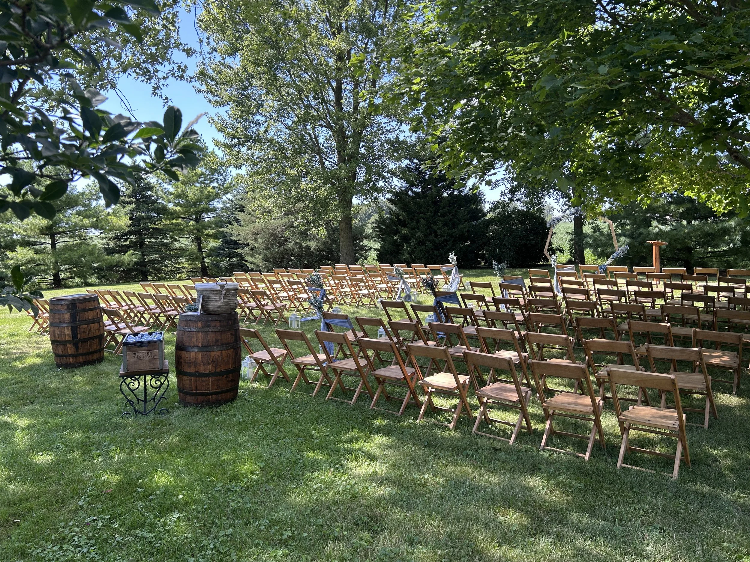 Rows of wooden chairs meticulously placed for an outdoor wedding ceremony at Country Coach House in Burlington, IL with blue and white country-rustic decor. 