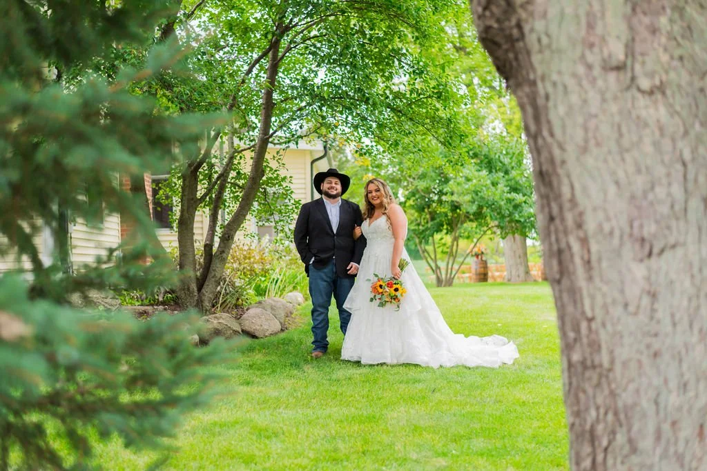 Bride and groom standing outside the white farmhouse surrounded by lush green landscape at Country Coach House wedding venue in Burlington, Illinois.