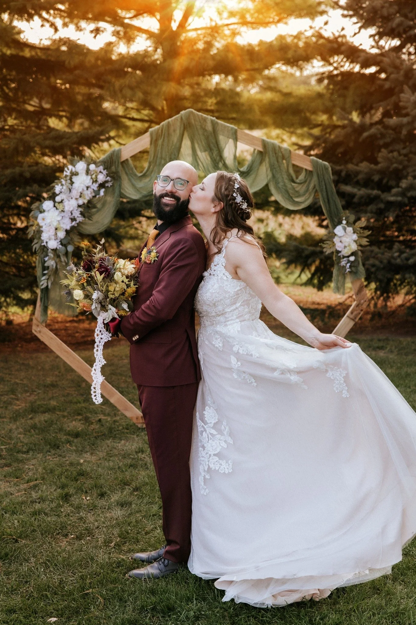 Bride kissing groom's cheek with heptogon arch backdrop at their wedding at Country Coach House, Burlington, IL