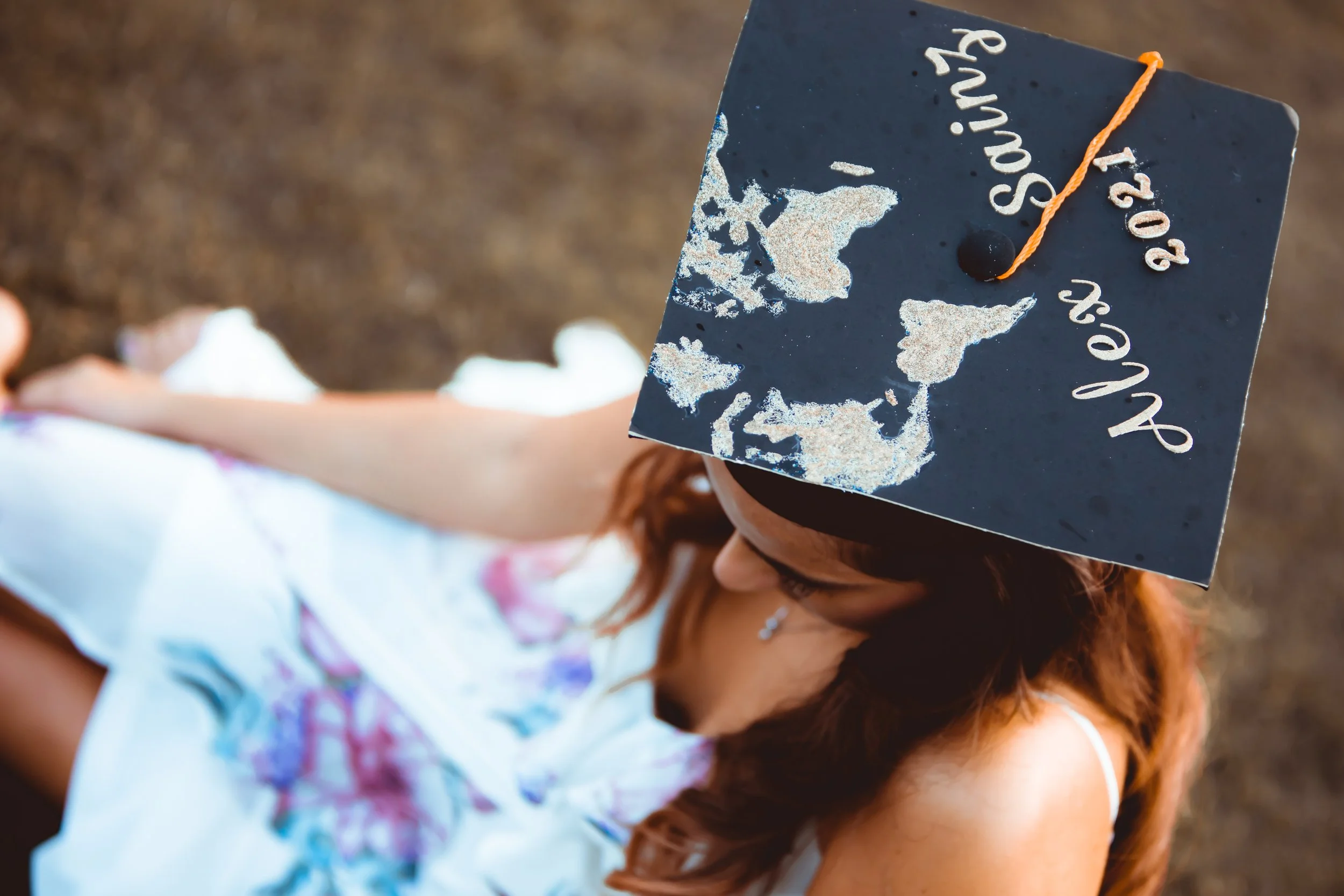 A person wearing a graduation cap with white decorative elements and the year '2023' on it, seen from above and slightly behind.