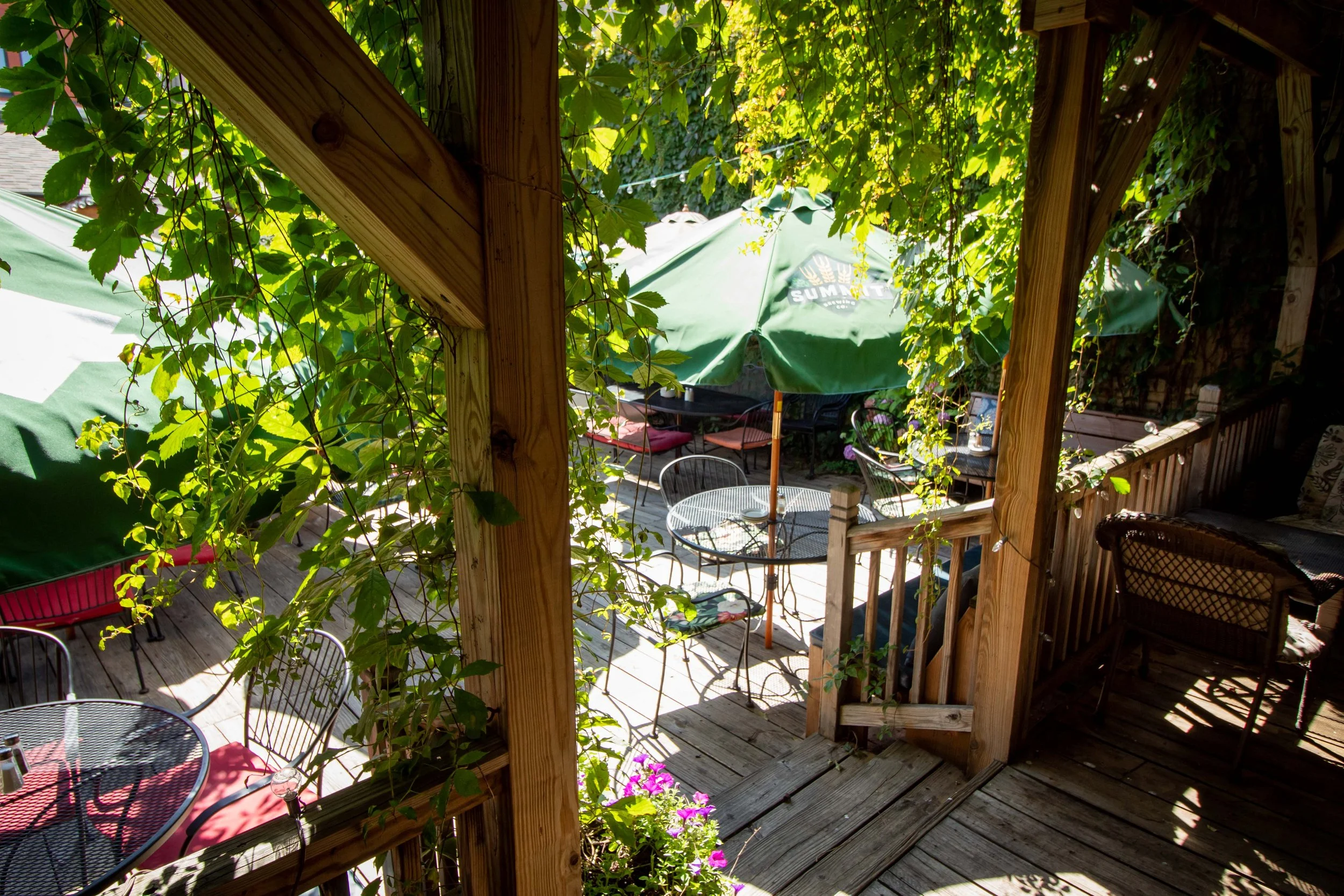 Outdoor cafe with greenery, wooden deck, tables, and chairs