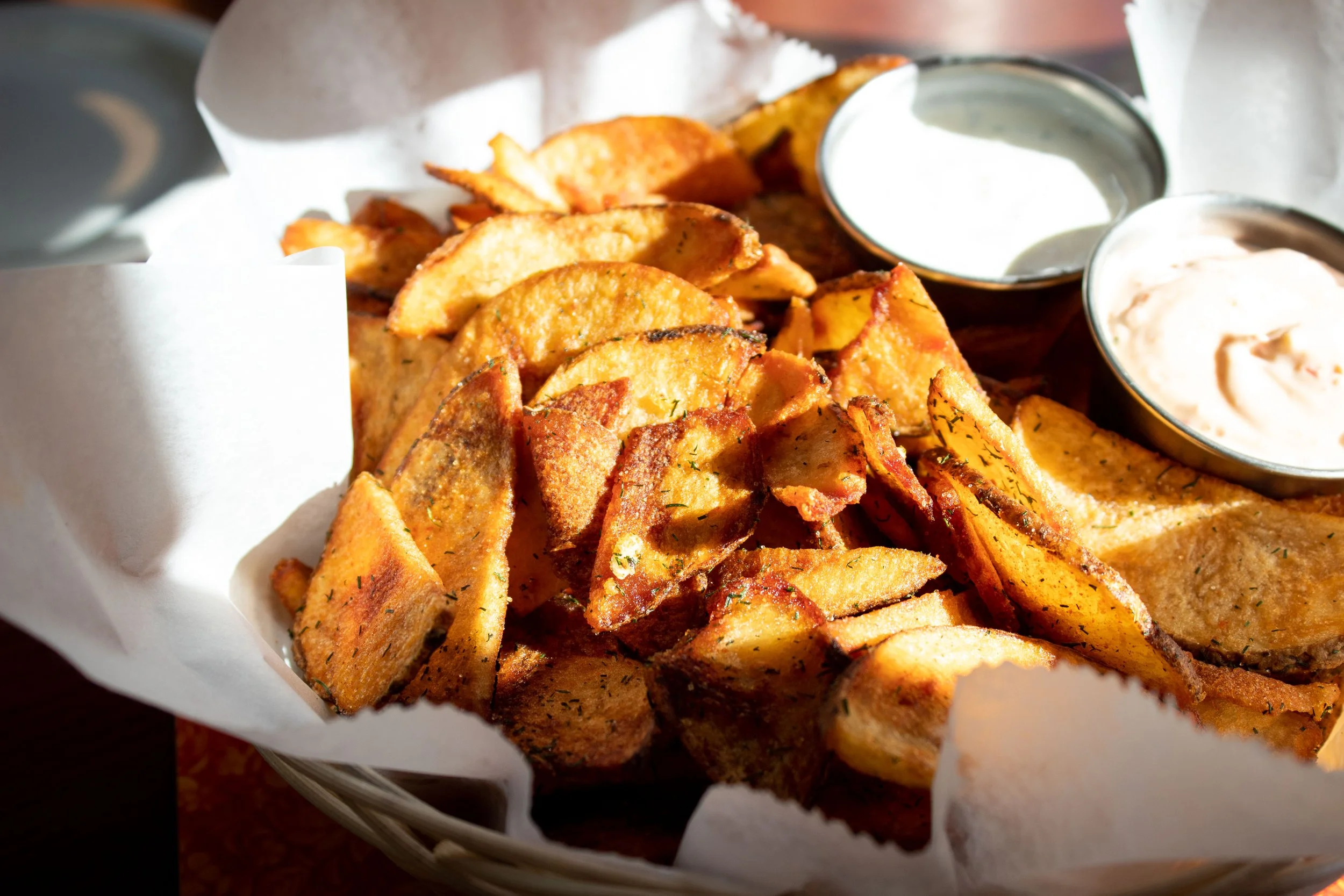Basket of seasoned potato wedges with two dipping sauces.
