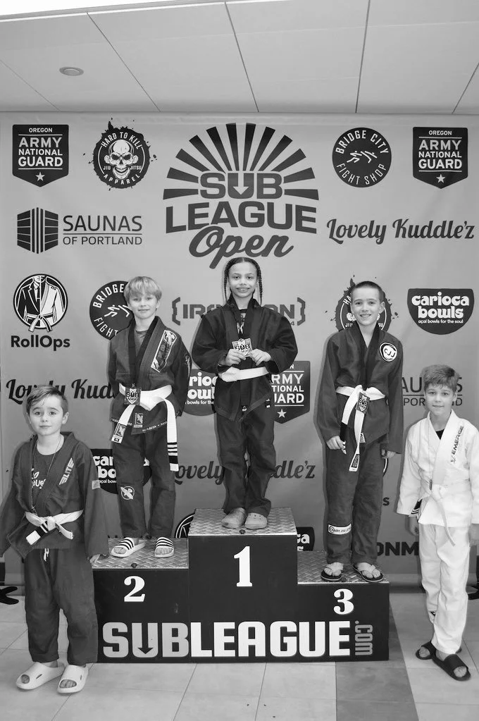 Kids BJJ team member standing atop podium in first place after winning his GI division at the 2026 Sub League Open