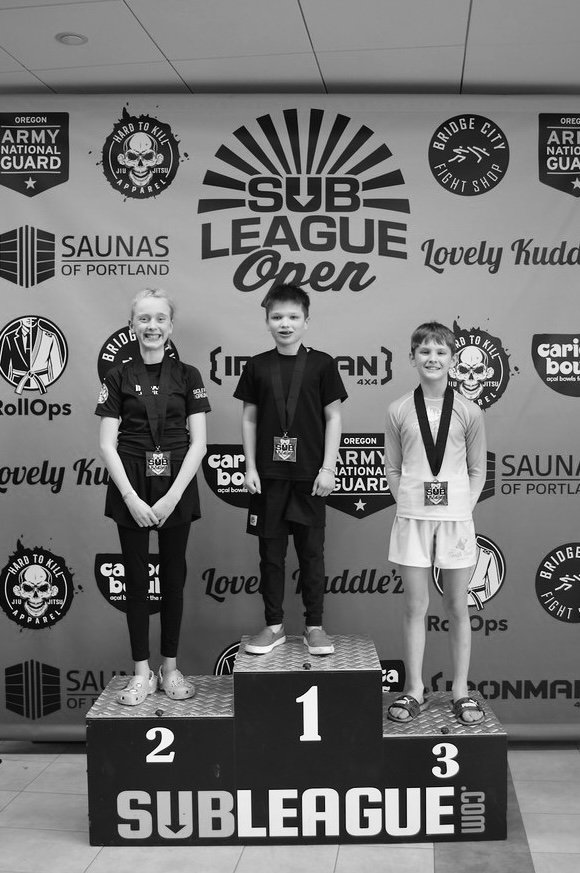 Oregon Grappling Arts kids jiu jitsu team member standing atop podium after placing first in his no gi bracket at the 2026 Sub League Open