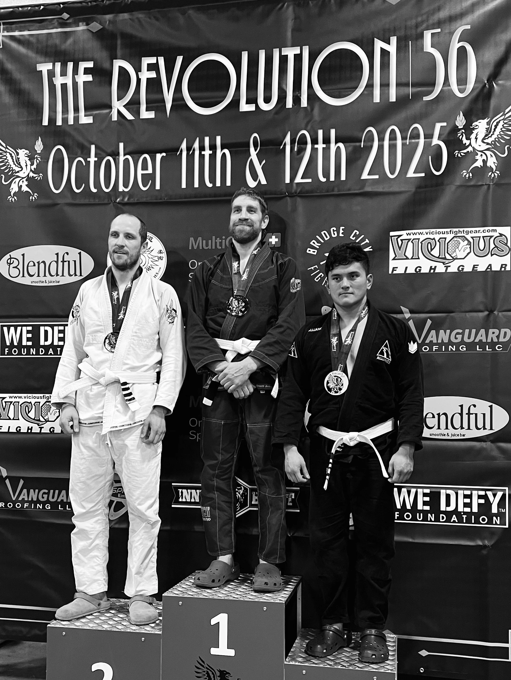 Adult jiu jitsu competitor standing in first place position atop podium after winning white belt gi BJJ bracket at the Revolution 56 tournament