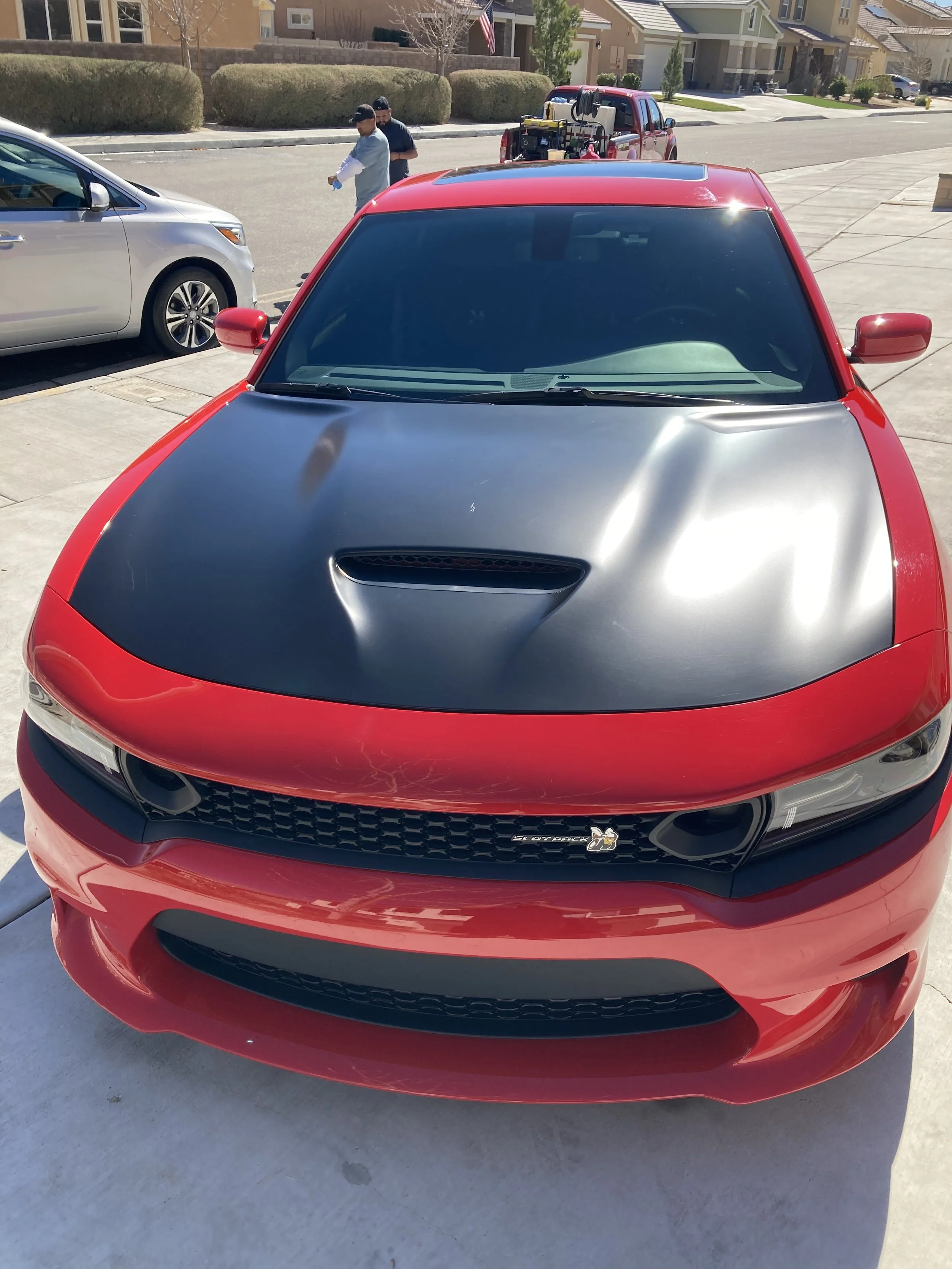 Front view of a red Dodge Charger with a black hood and custom blacked-out headlights, parked in a driveway.