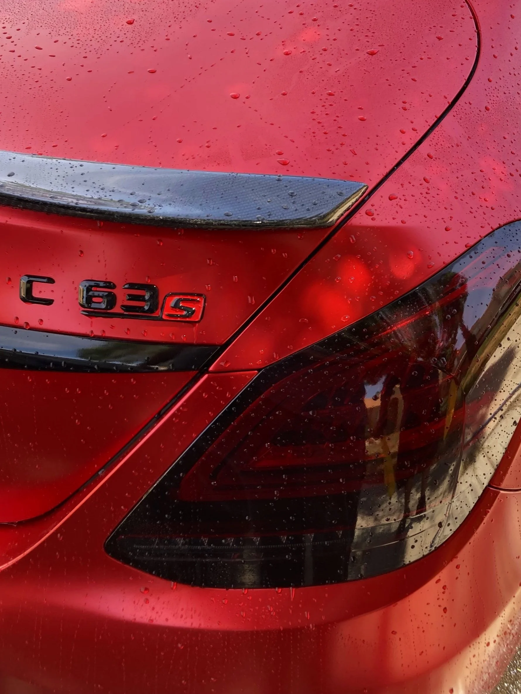 Close-up of the rear section of a red Mercedes-Benz C 63 S car with raindrops on the surface.