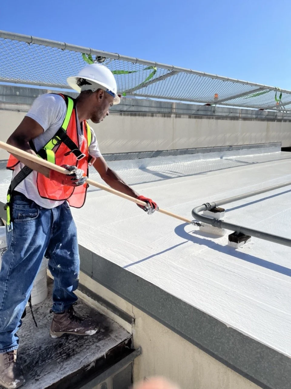 Crew member applying a coating to a flat commercial roof