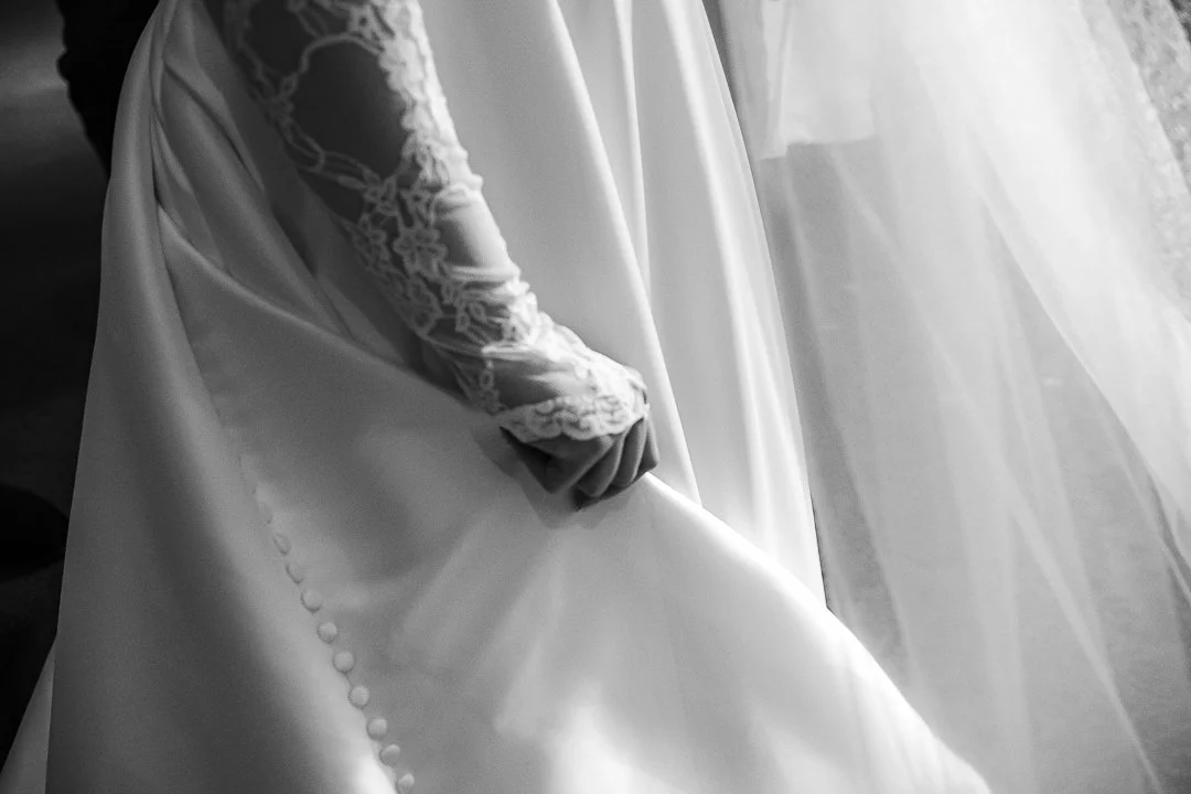 A bride with lace sleeves holding the hem of her wedding dress.