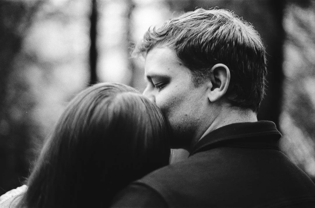 A man kissing a woman on the forehead outdoors, black and white photo.