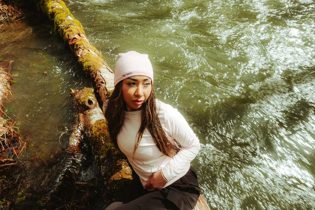 Woman in white and black sitting by a moss-covered fallen tree in a river.