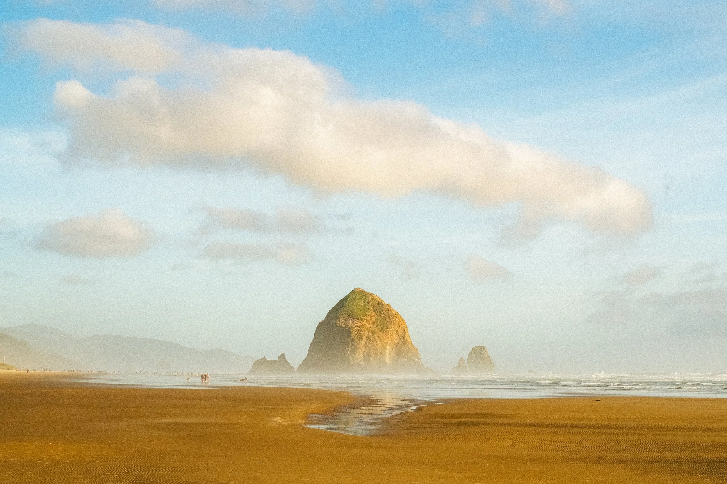 A scenic view of a beach with a large rocky formation in the water, and a cloudy sky overhead.