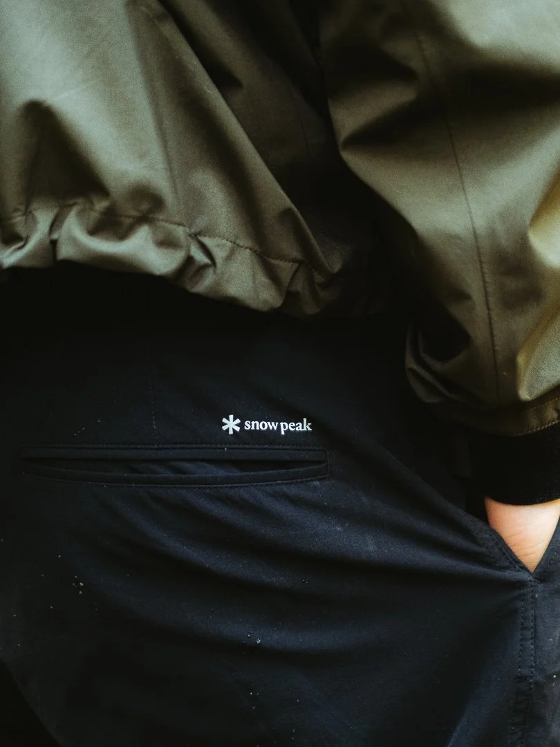 Close-up of a person wearing a green jacket and black pants with a Snow Peak logo visible on the pocket area.