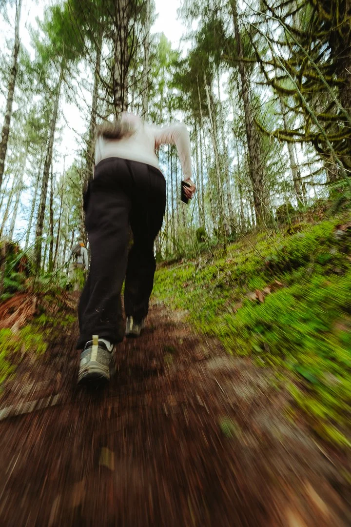 Person hiking in a forest on a muddy trail, seen from behind.