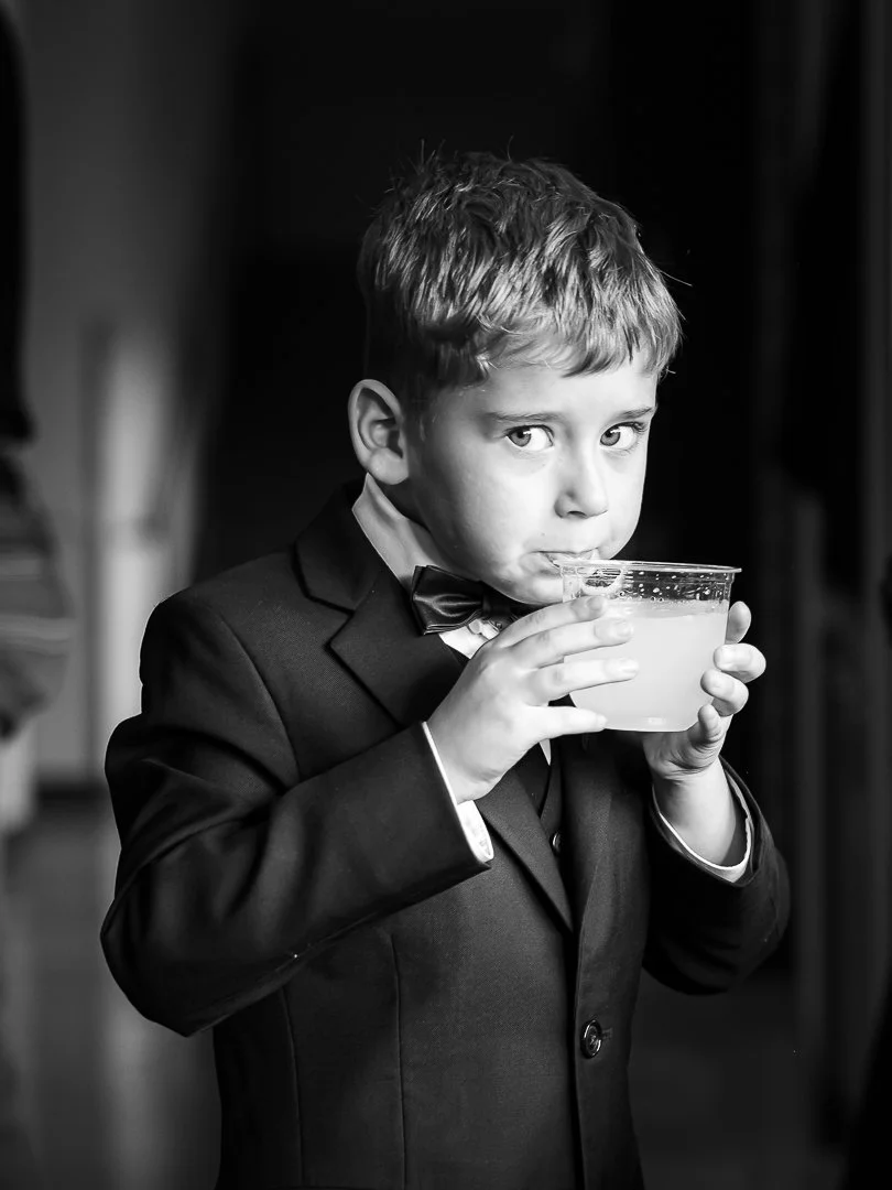 A young boy in a suit and bow tie drinking from a glass bowl of lemonade.