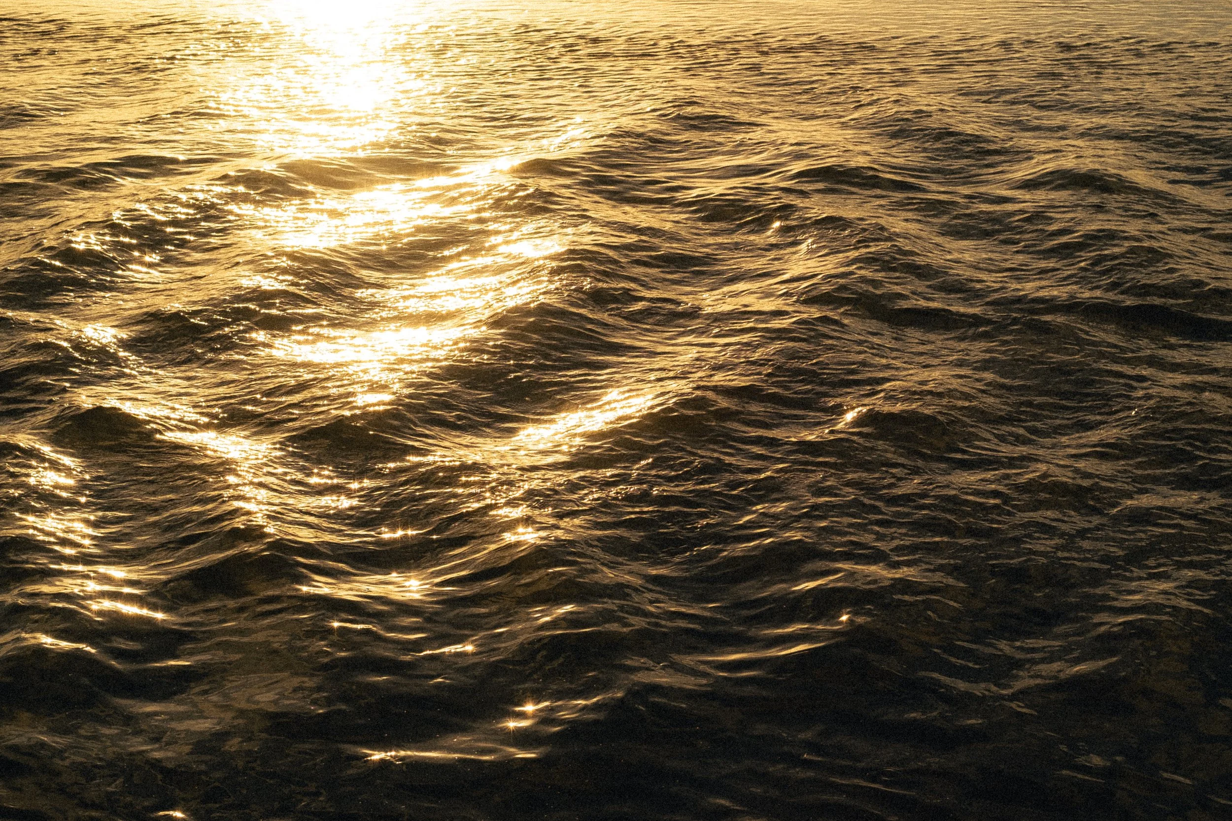 Golden sunlight reflecting on the ocean with rippling water surface.