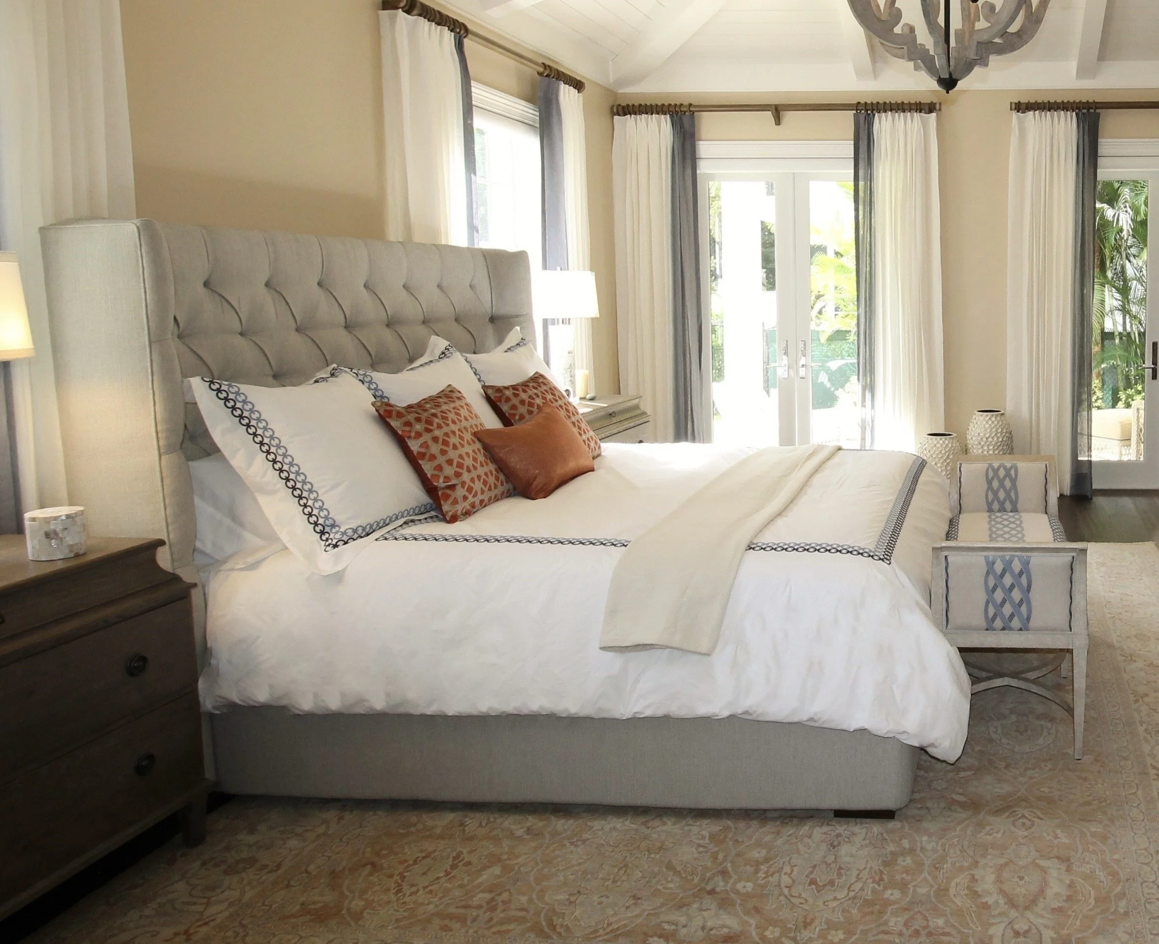 bedroom with a tufted headboard, white bedding, and decorative pillows, accented by natural light from large windows.