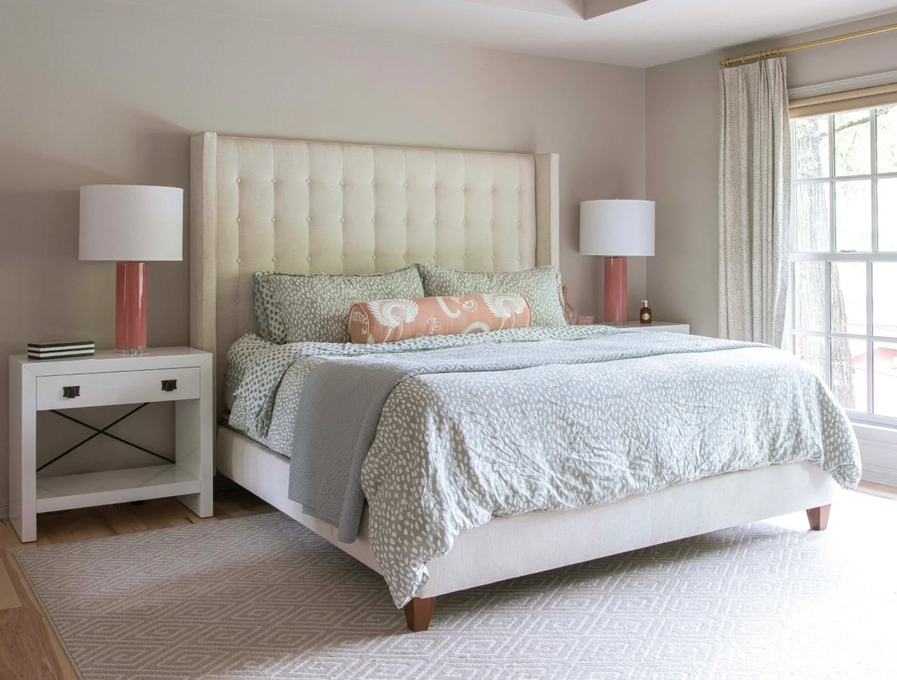 Bed with patterned linens and a white, tufted headboard. There is a soft, patterned rug under the bed.