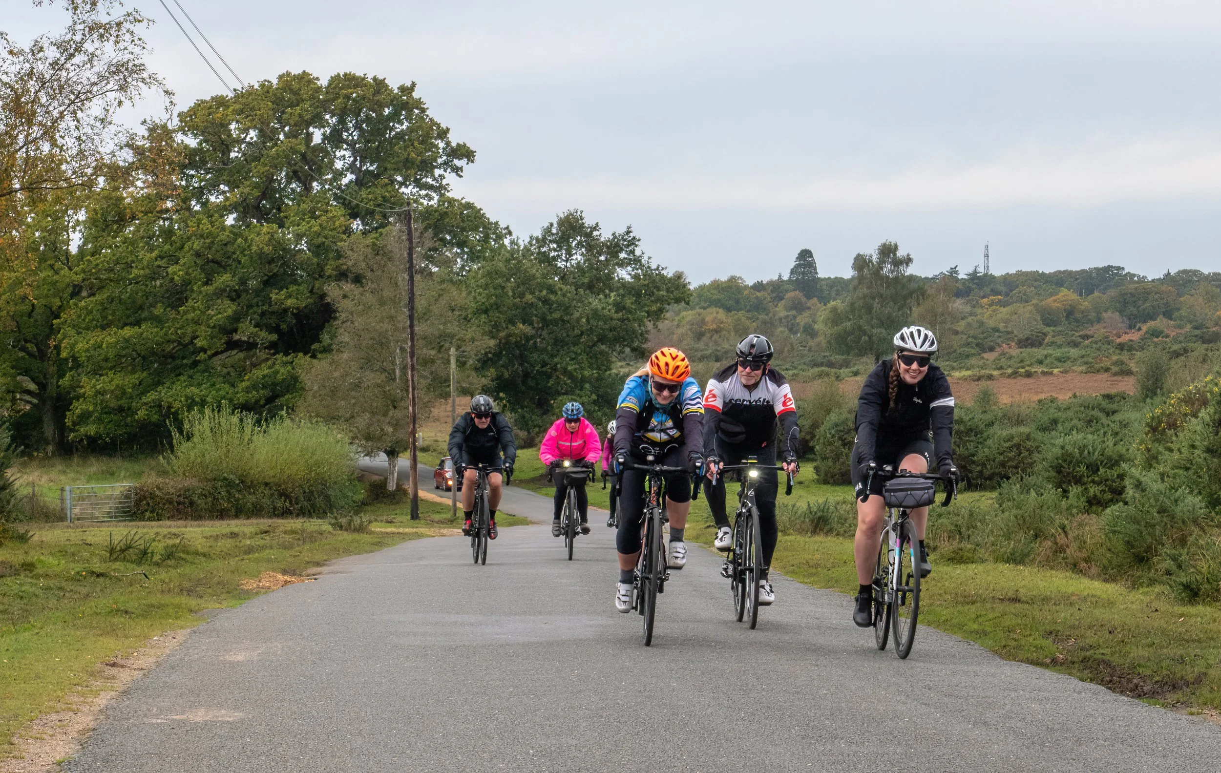 A group of cyclists riding on a paved path in a green rural area with trees and rolling hills in the background