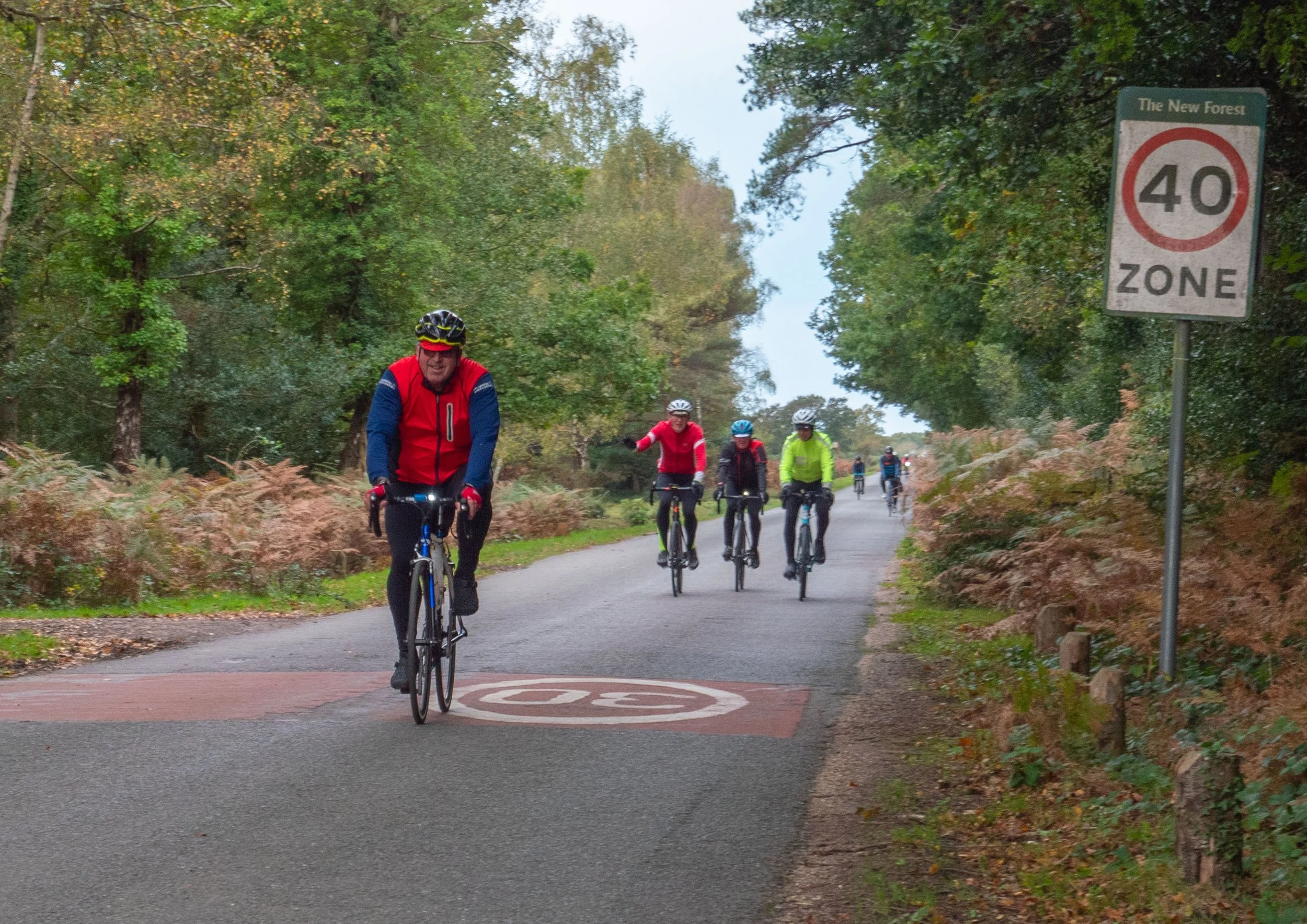 A group of cyclists riding on a forested path with trees on both sides and a speed zone sign indicating 40 km/h.