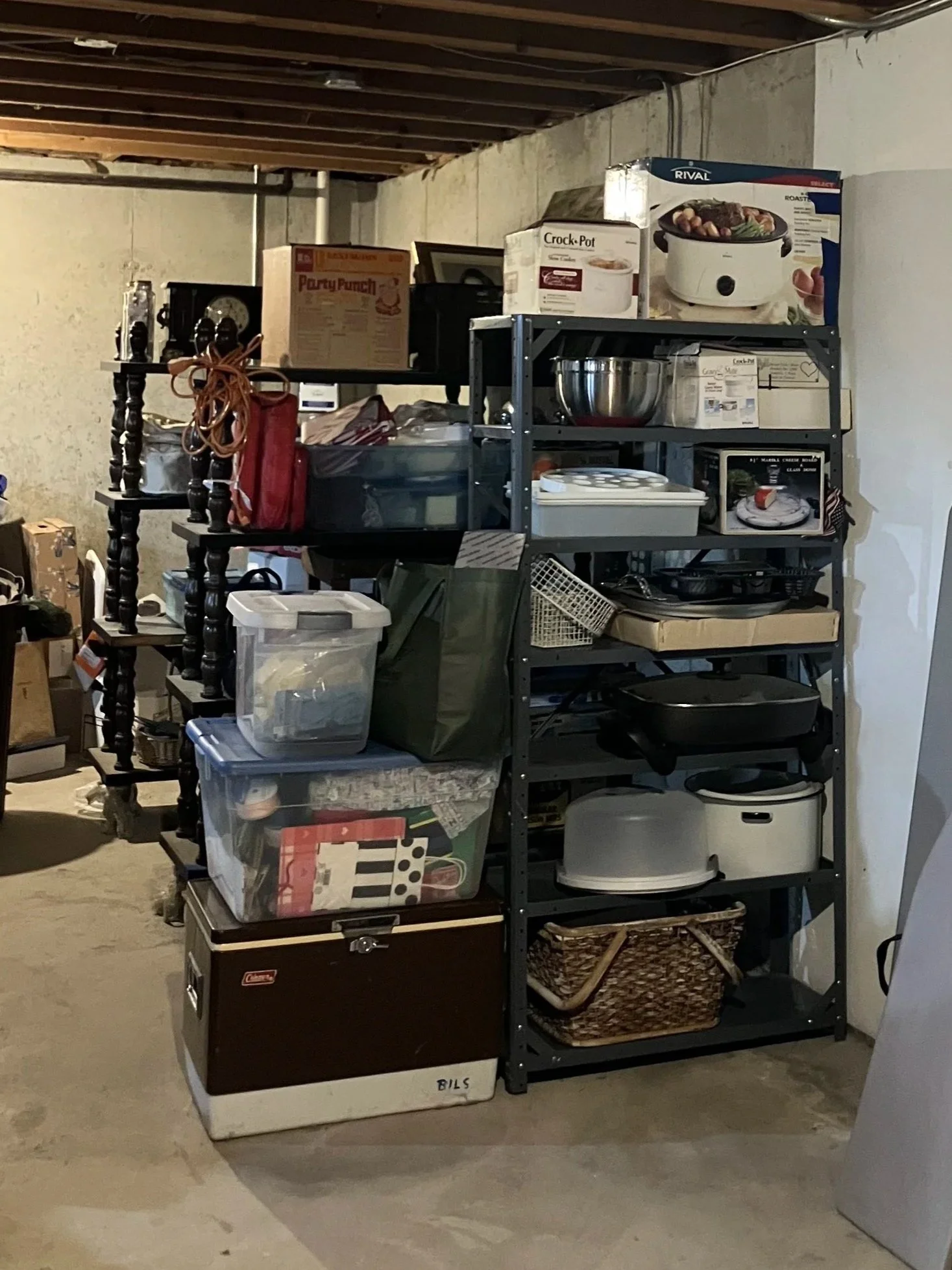 Shelving unit and plastic storage bins in a basement or storage room, holding various kitchen appliances, boxes, and miscellaneous items.