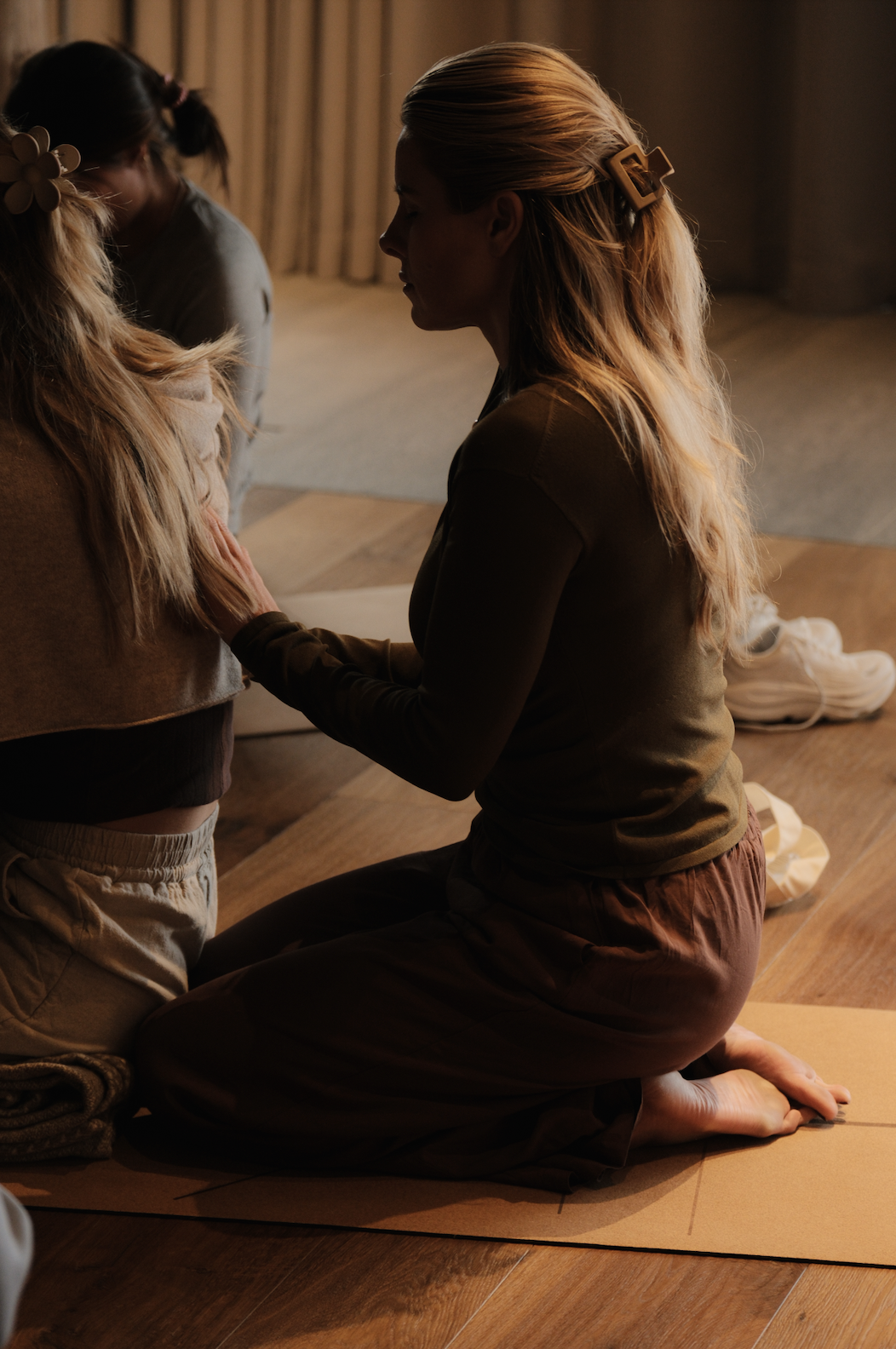 A woman kneeling on the floor with her eyes closed, holding a young girl's hands during a prayer or mindful moment.