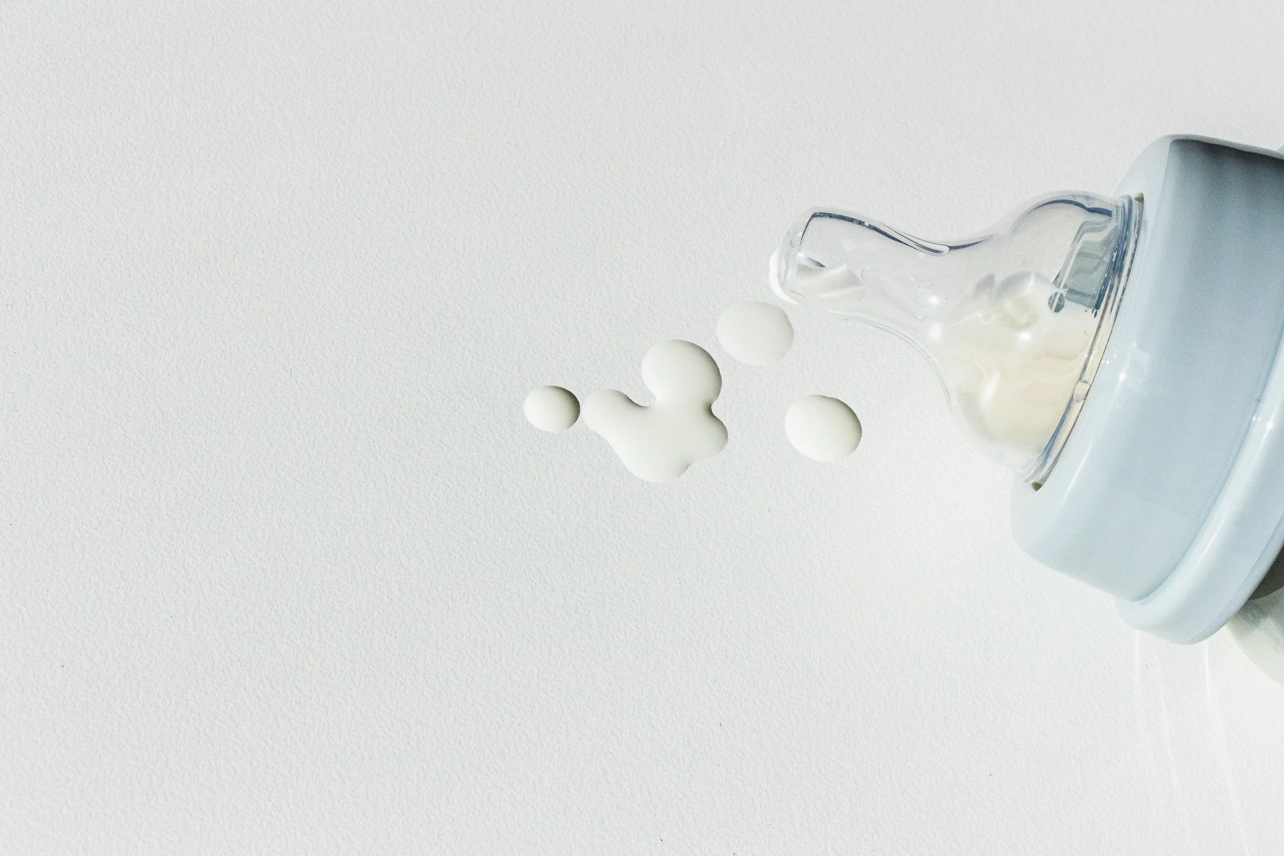 Plastic bottle pouring white foam or foam-like substance into a clear container on a white surface.